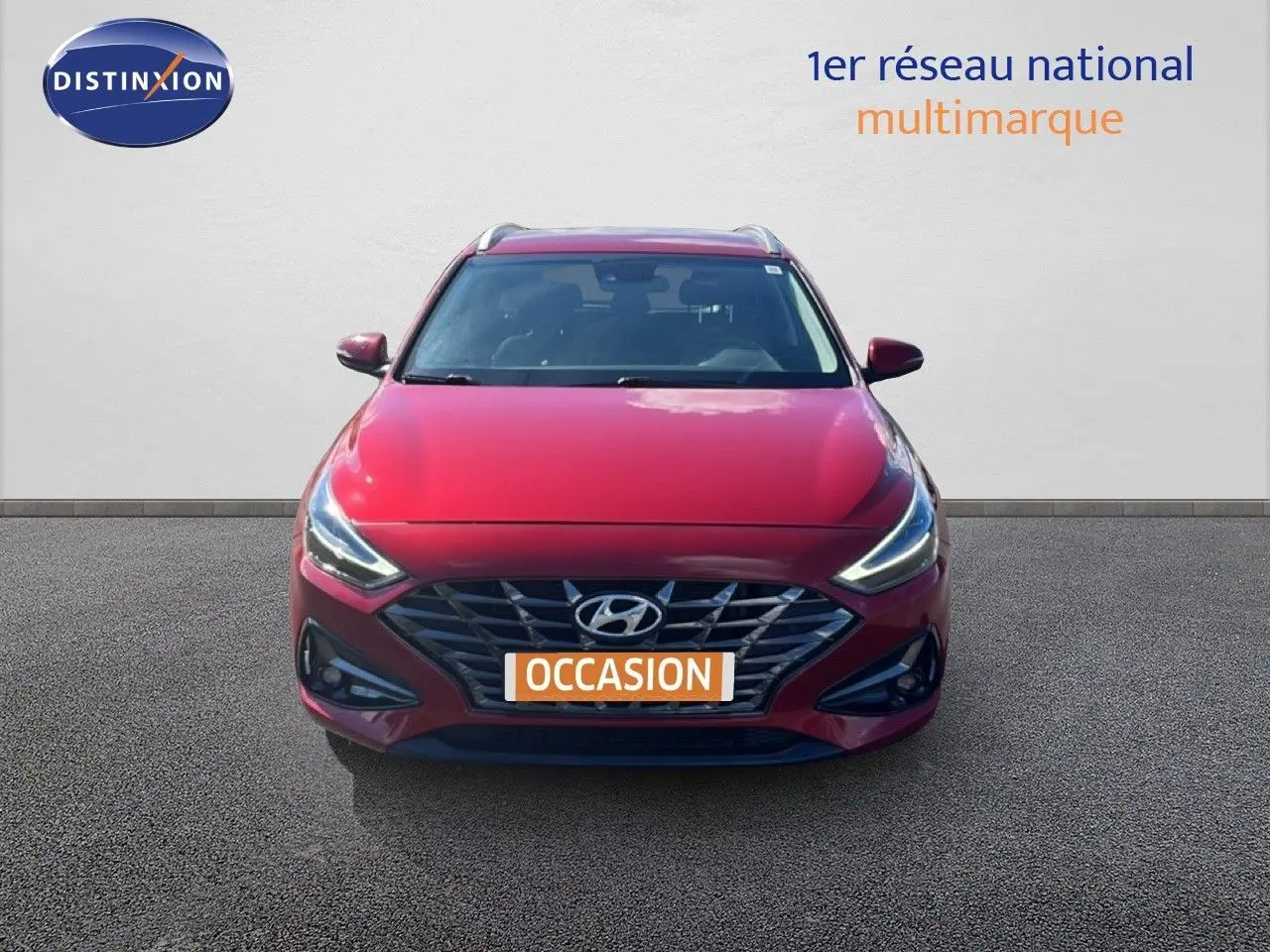 Vue frontale d'une Hyundai i30 SW 2023 rouge Sunset Red Metal avec calandre distinctive et phares LED allumés.
