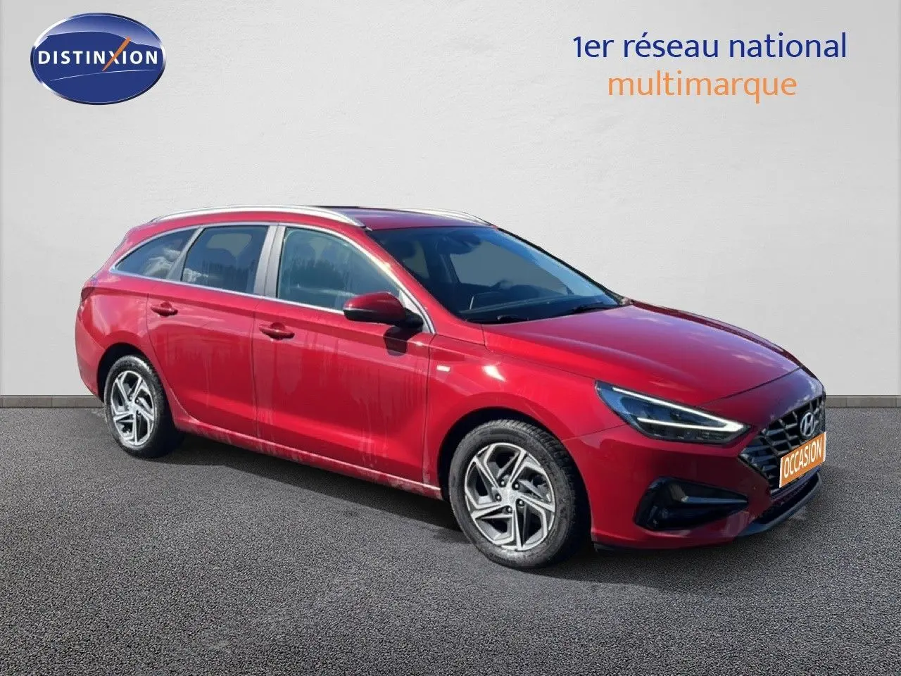 Hyundai i30 SW 2023 rouge Sunset Red Metal vue 3/4 avant droit avec jantes alliage biton et feux LED allumés.