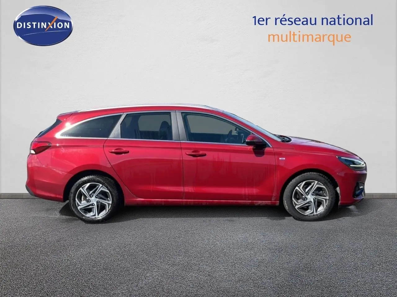 Profil droit d'une Hyundai i30 SW 2023 rouge Sunset Red Metal avec jantes alliage et toit ouvrant visible.