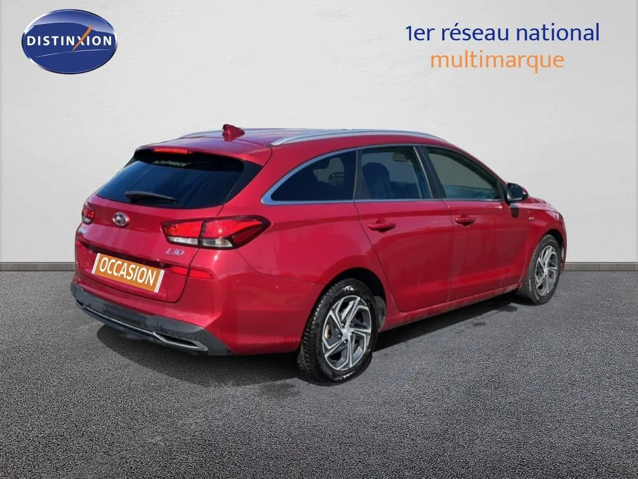Vue 3/4 arrière droite d'une Hyundai i30 SW 2023 rouge Sunset Red Metal avec jantes bi-ton et feux LED.