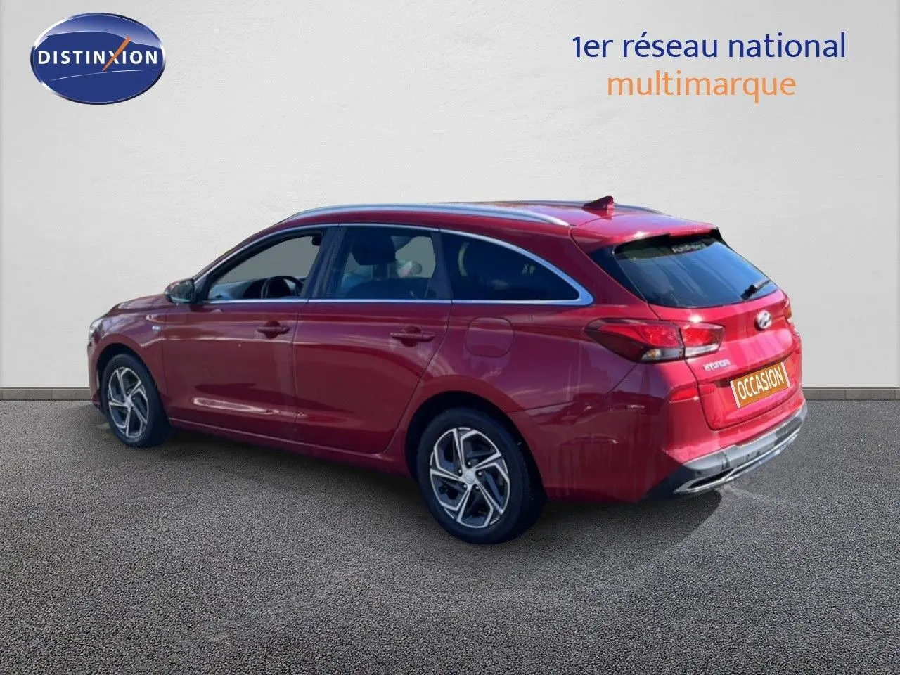 Vue 3/4 arrière droite d'une Hyundai i30 SW 2023 rouge Sunset Red Metal avec jantes alliage et toit panoramique.