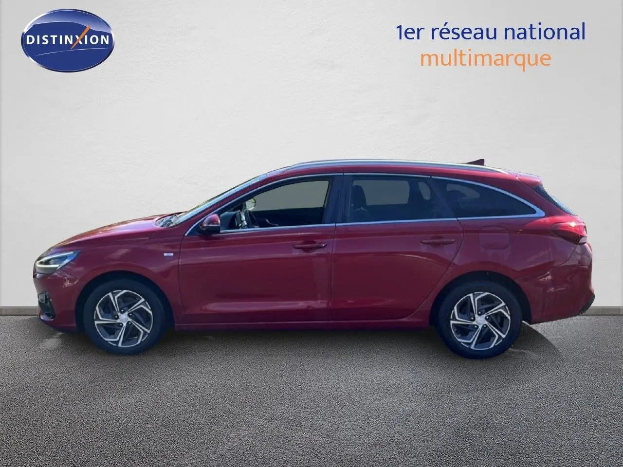 Vue de profil côté gauche d'une Hyundai i30 SW 2023 rouge Sunset Red Metal avec jantes bi-ton et vitres teintées.