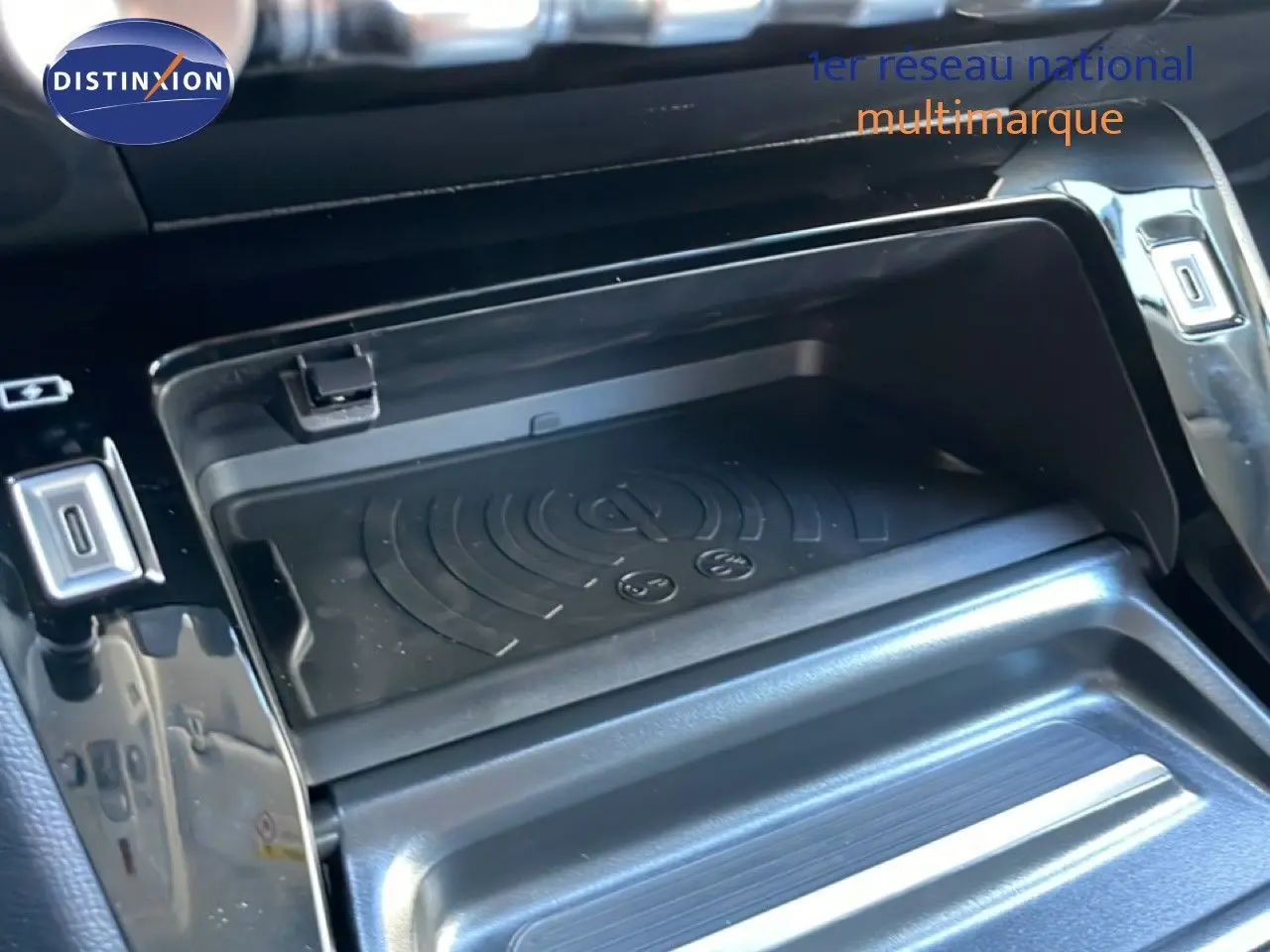 Gros plan sur le compartiment de recharge sans fil au centre de la console d’une Peugeot 208 Hybrid 110ch noire.
