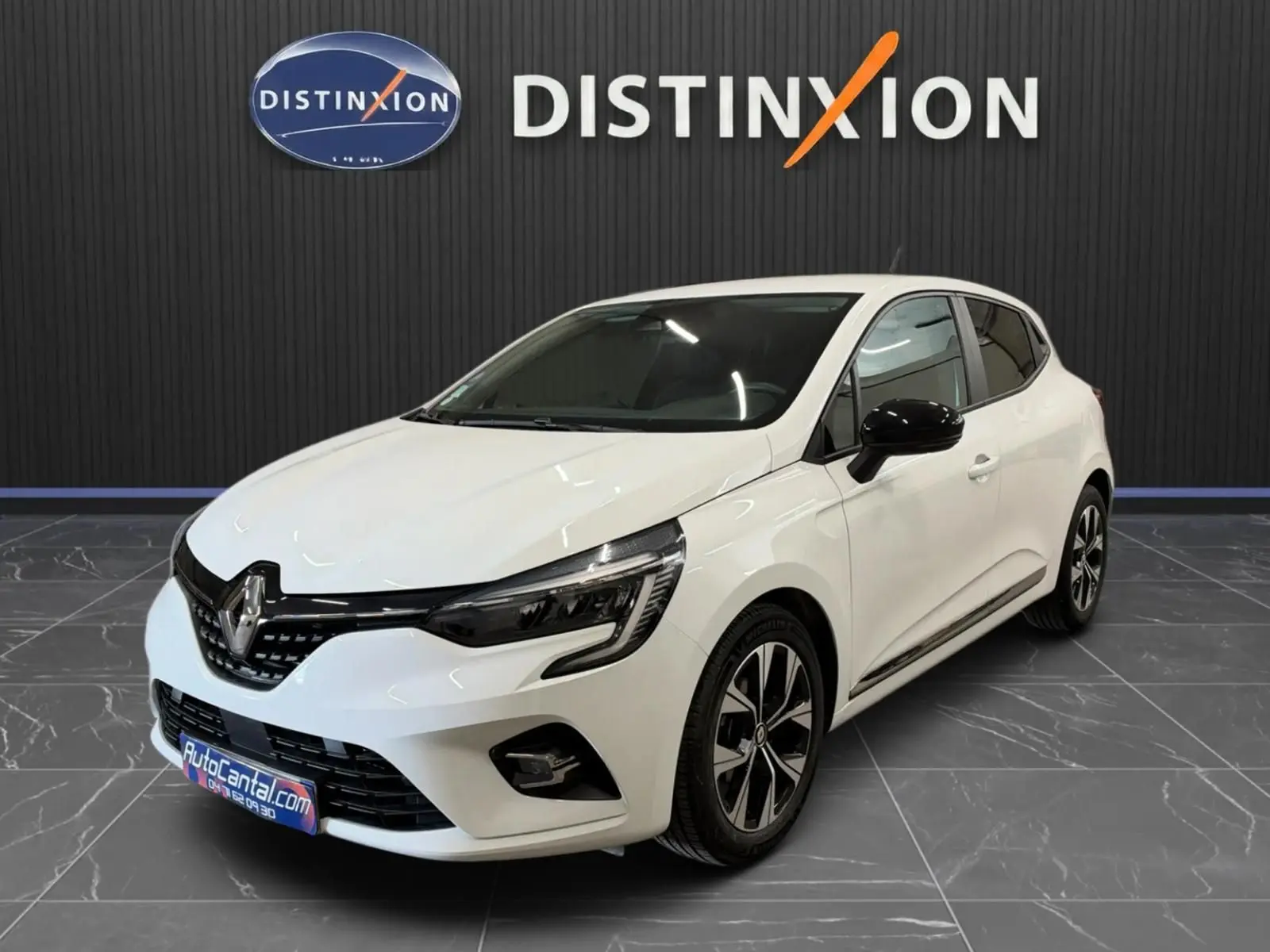 Renault Clio V blanche vue 3/4 avant droit, jantes bi-ton et rétroviseurs noirs, stationnée en intérieur showroom.