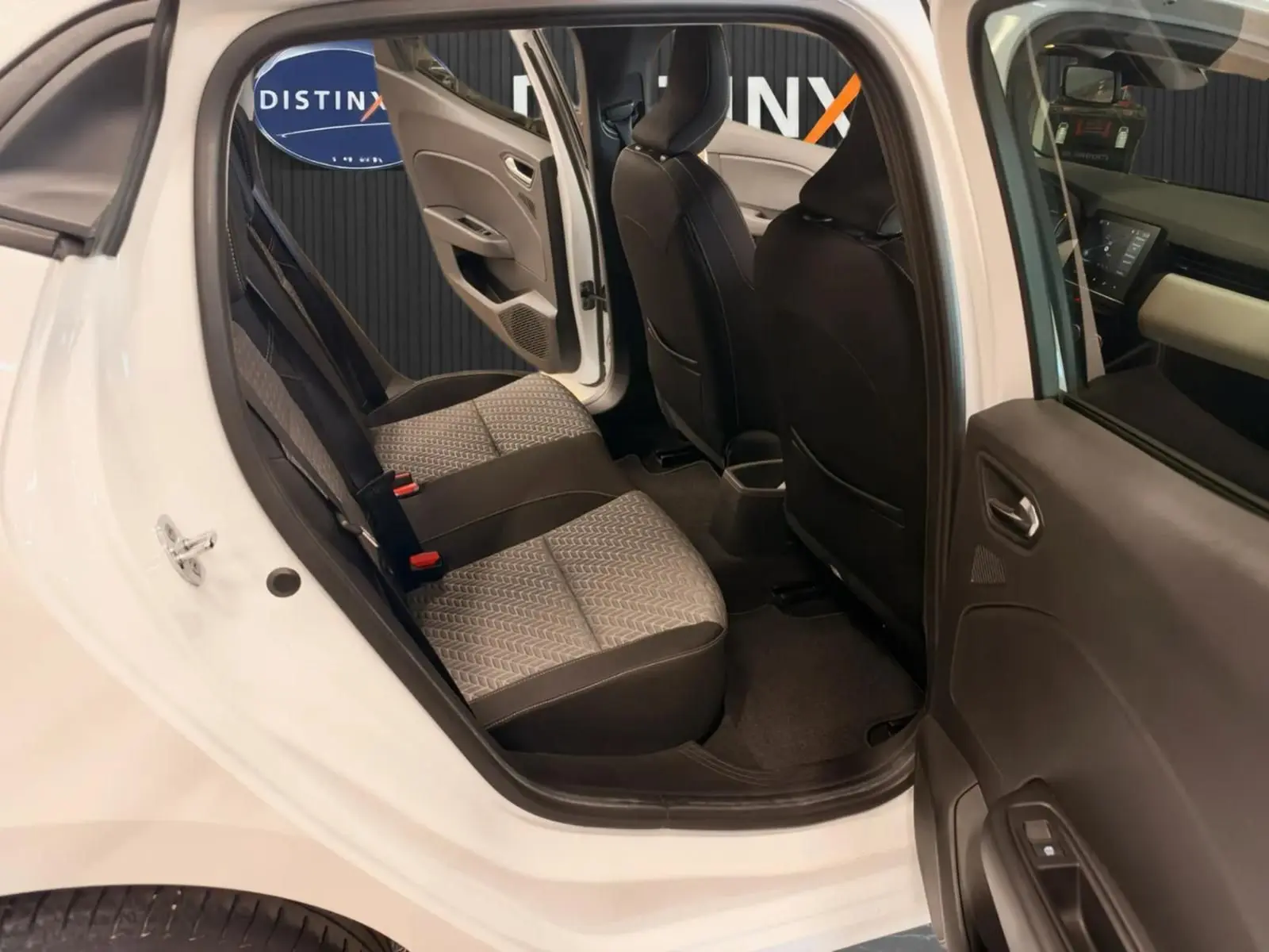 Vue intérieure côté gauche arrière de la Renault Clio V blanche, montrant les sièges arrière en tissu gris et noir.