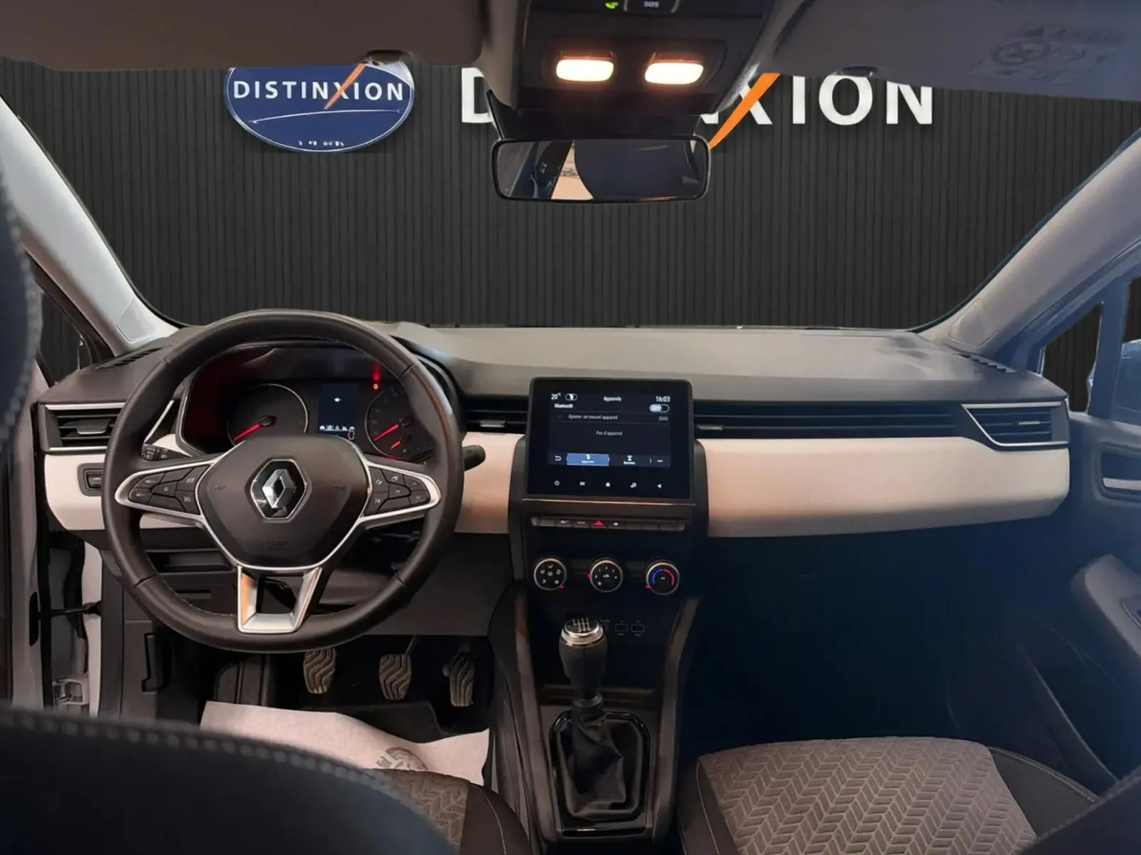 Vue intérieure avant de la Renault Clio V blanche, tableau de bord gris clair avec écran tactile et volant multifonction.