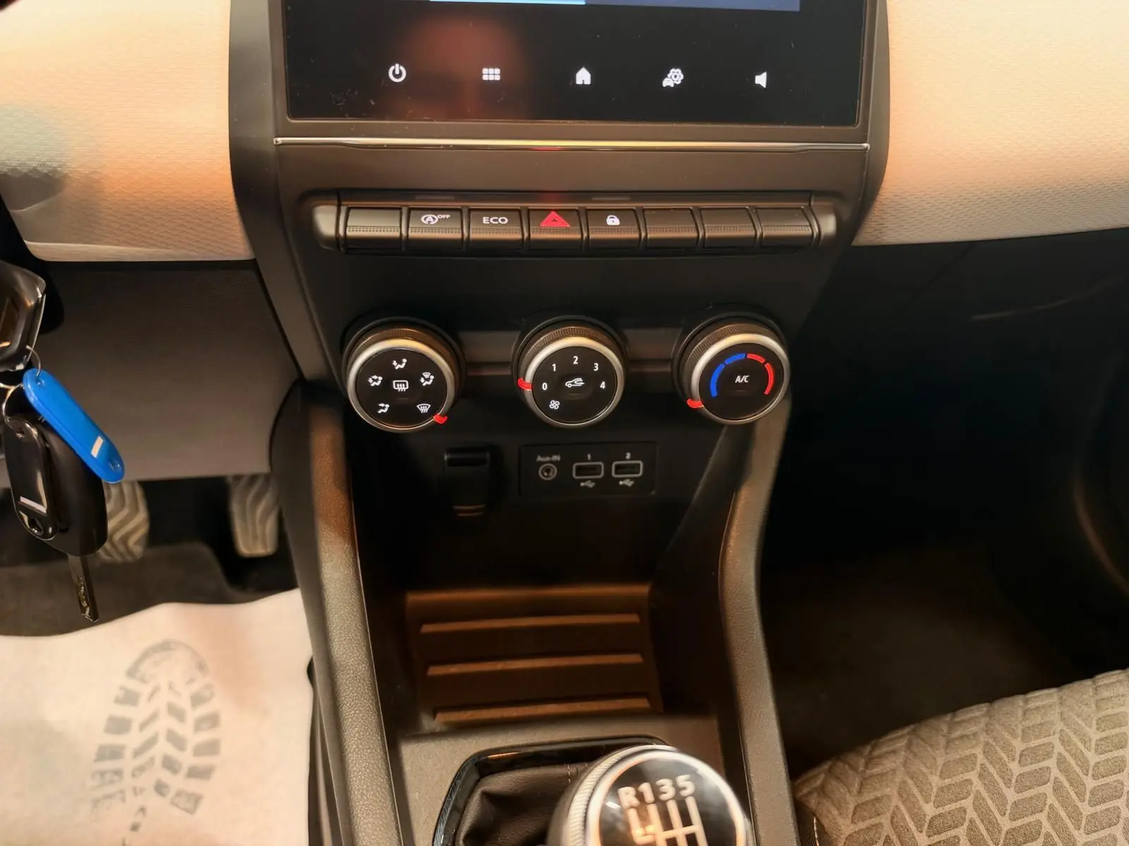 Vue rapprochée du tableau de bord et de la console centrale de la Renault Clio V blanche, avec commandes de climatisation et levier de vitesses manuel.