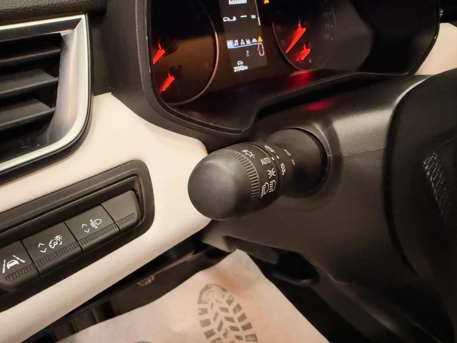 Détail du commodo d’éclairage et tableau de bord partiel de la Renault Clio V blanche, intérieur gris.