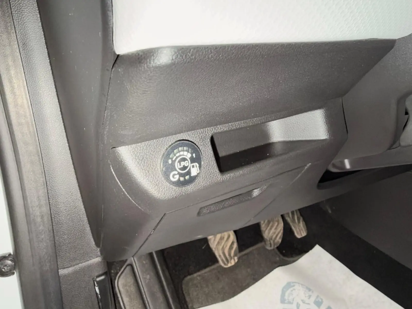 Détail intérieur montrant le bouton de sélection GPL sous le tableau de bord côté conducteur de la Renault Clio V blanche.