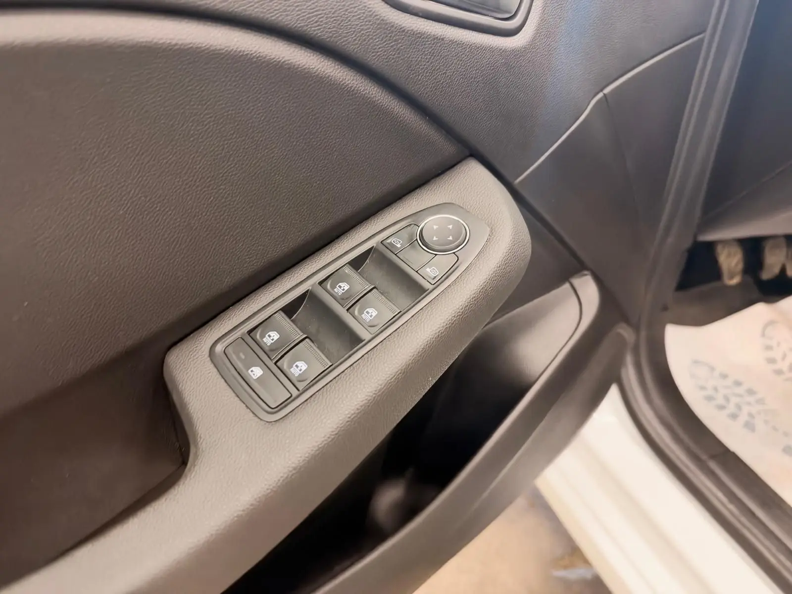 Gros plan sur la commande des vitres côté conducteur de la Renault Clio V blanche, avec portière ouverte.
