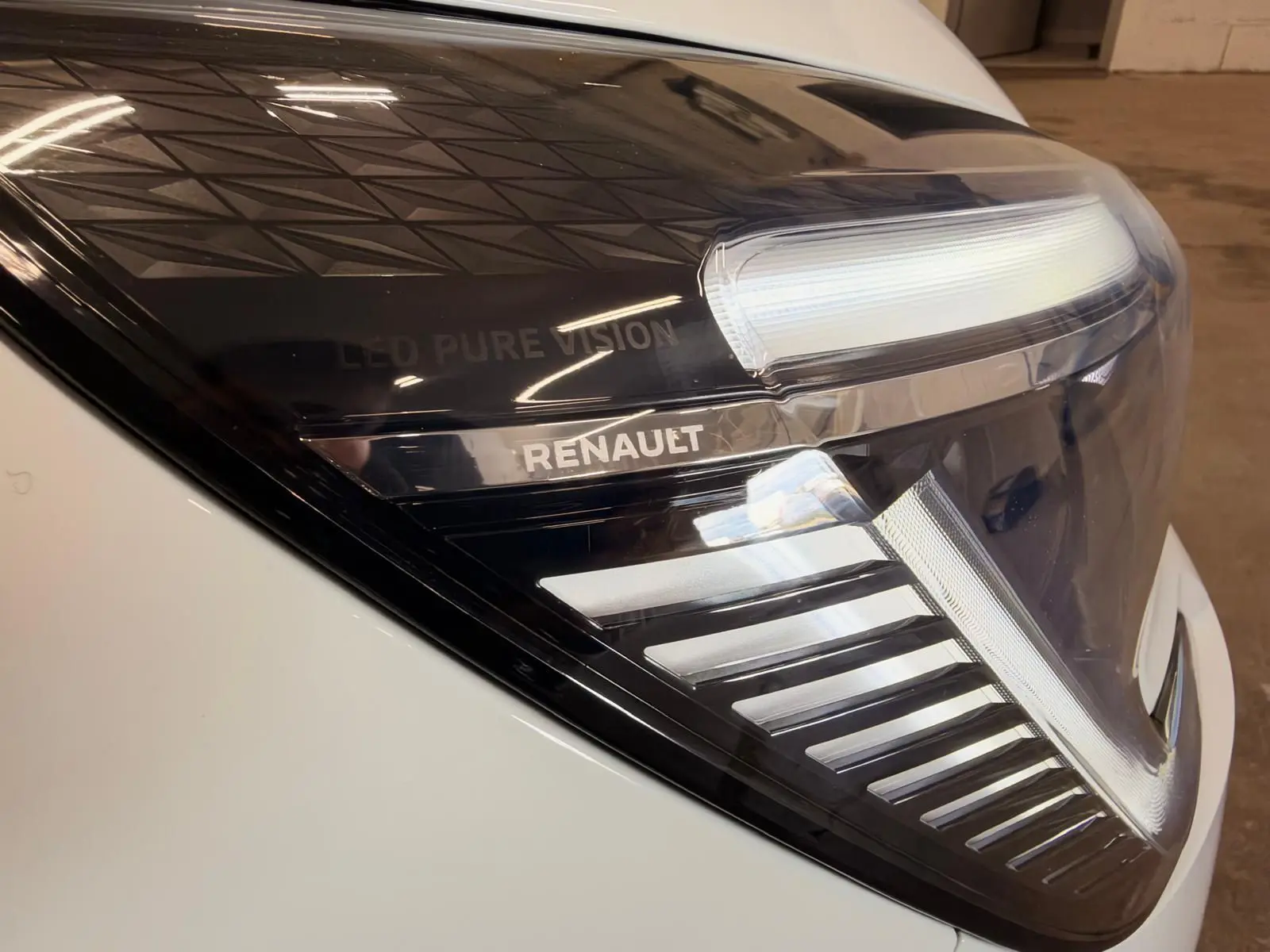 Gros plan sur le phare avant droit blanc de la Renault Clio V avec marquage LED Pure Vision et logo Renault visible.