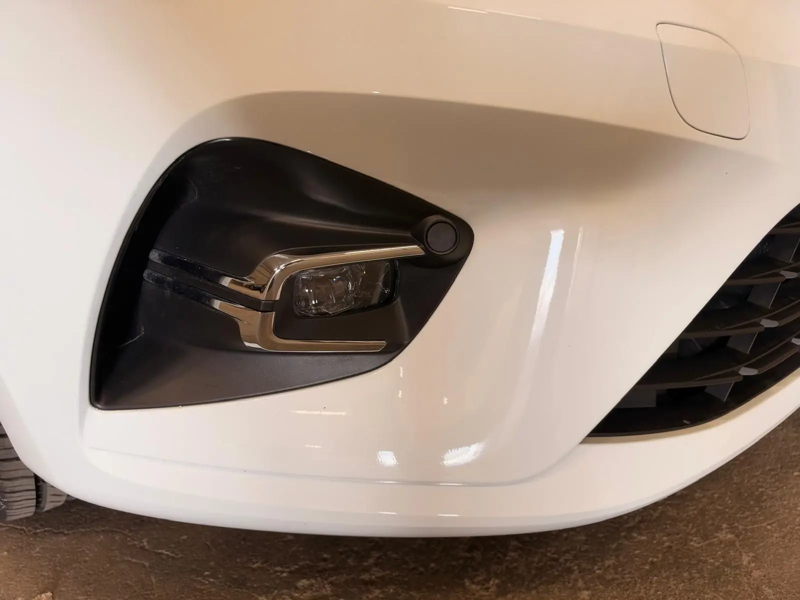 Gros plan sur le feu antibrouillard avant gauche de la Renault Clio V blanche, avec détails chromés et calandre partielle visible.