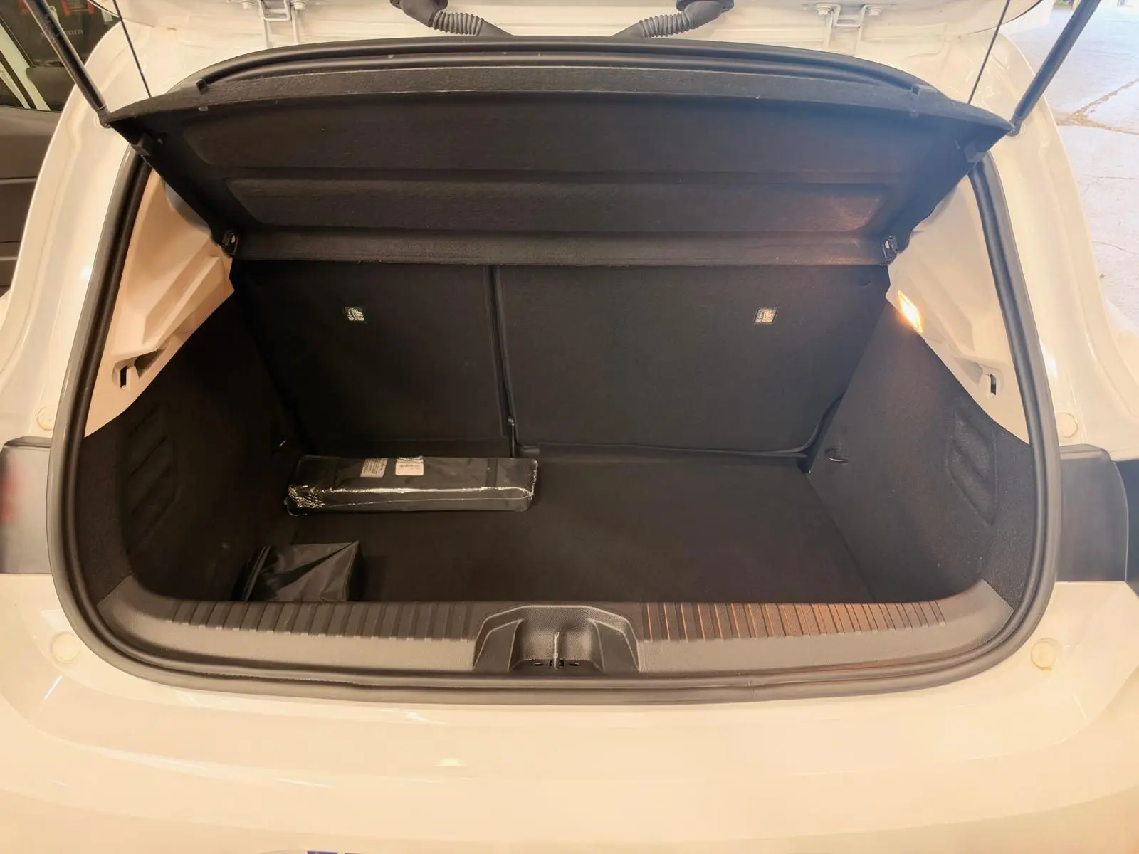 Coffre ouvert d'une Renault Clio V blanche, vue arrière, montrant un espace de rangement propre et éclairé.