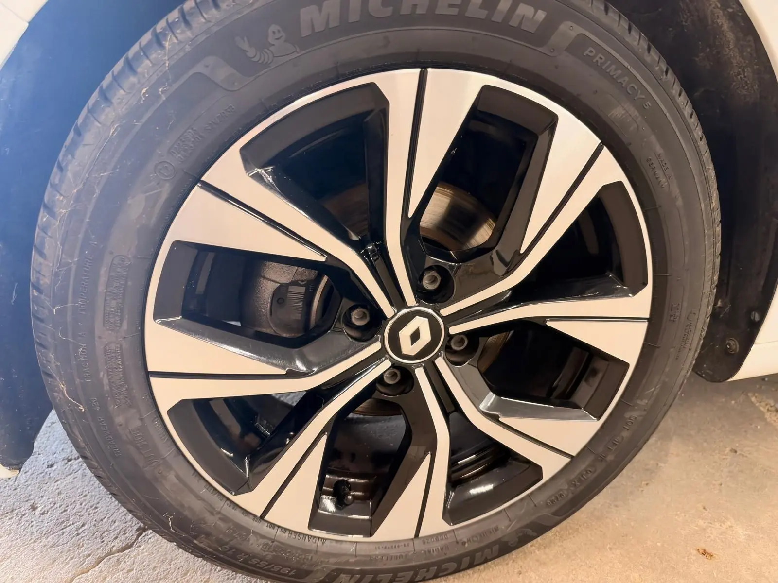 Gros plan sur la jante alliage bicolore noire et argentée d'une Renault Clio V blanche, roue avant droite.
