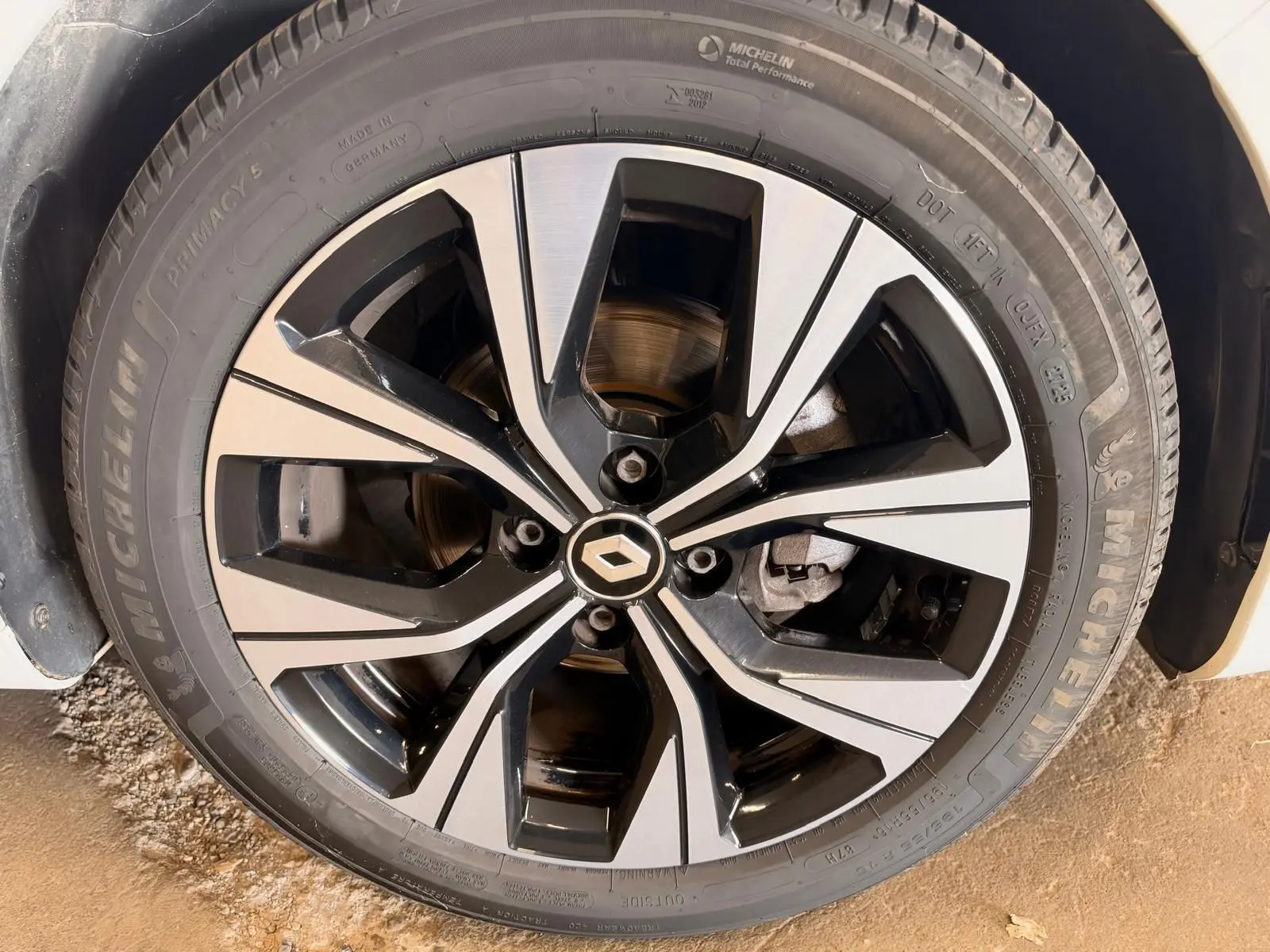 Gros plan sur la jante alliage bicolore noire et argentée avec logo Renault, pneu Michelin, sur Clio V blanche.