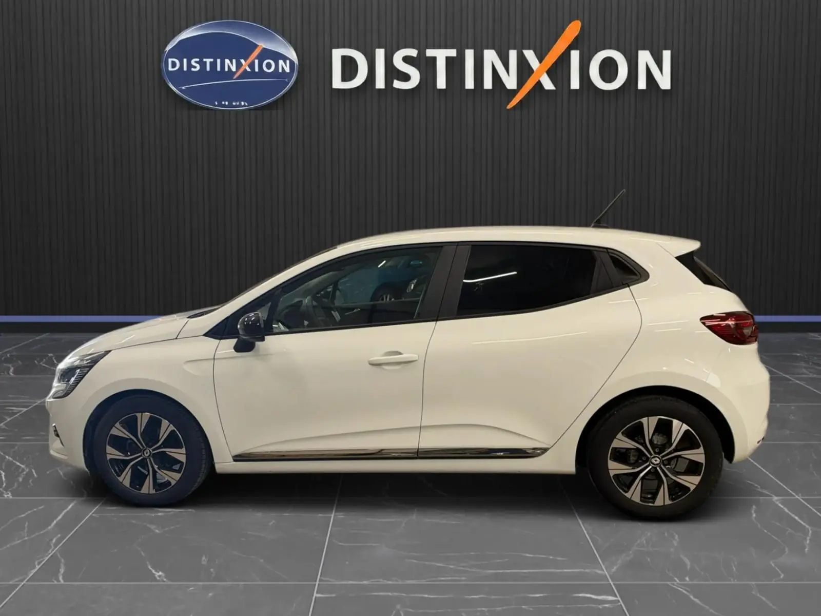 Profil côté gauche d'une Renault Clio V blanche 5 portes avec jantes bi-ton et vitres teintées, en intérieur showroom.