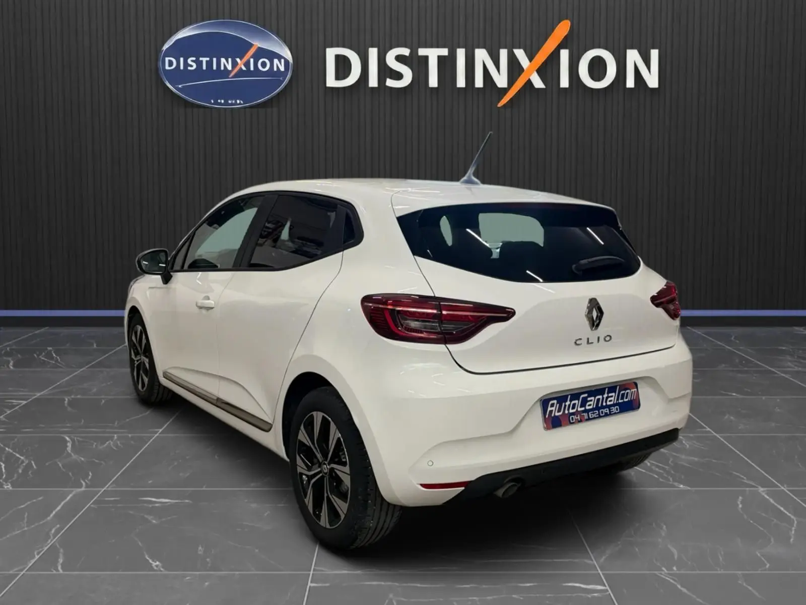 Vue 3/4 arrière droite d'une Renault Clio V blanche, avec jantes bi-ton et vitres teintées, en intérieur showroom.
