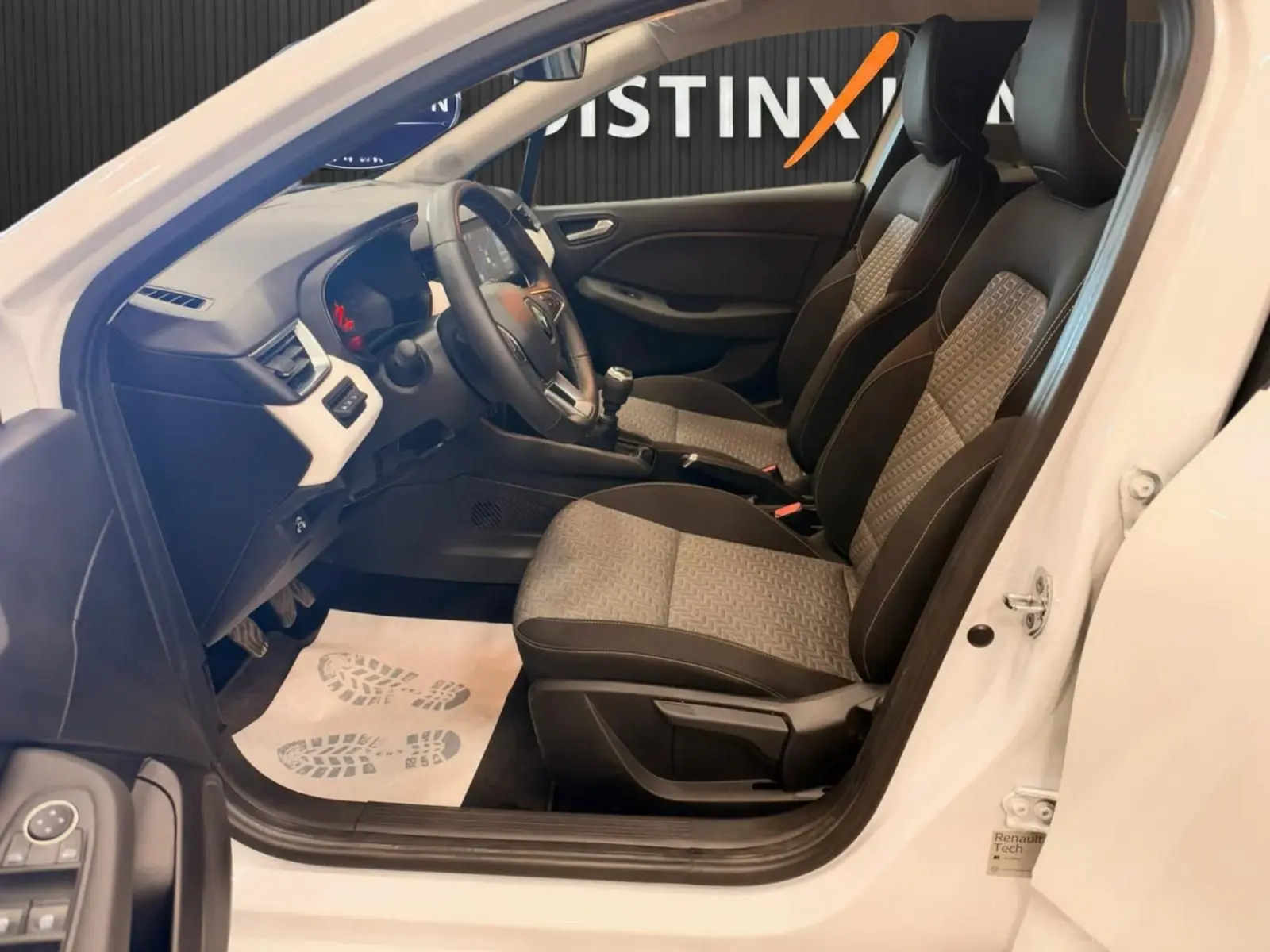 Intérieur de la Renault Clio V blanc vue côté gauche, sièges bi-ton gris et noir avec volant et tableau de bord visibles.