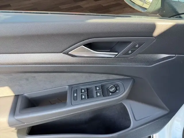 Vue rapprochée de la porte côté conducteur d'une Volkswagen Golf blanche, mettant en valeur les commandes électriques et la poignée intérieure.