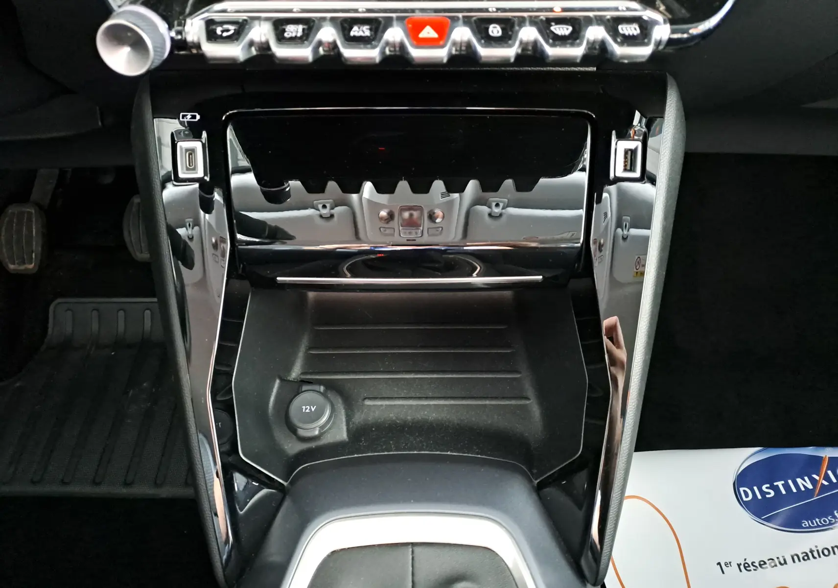 Gros plan sur la console centrale noire brillante du Peugeot 2008 1.2 PureTech 100 Allure, avec prise 12V et commandes tactiles.