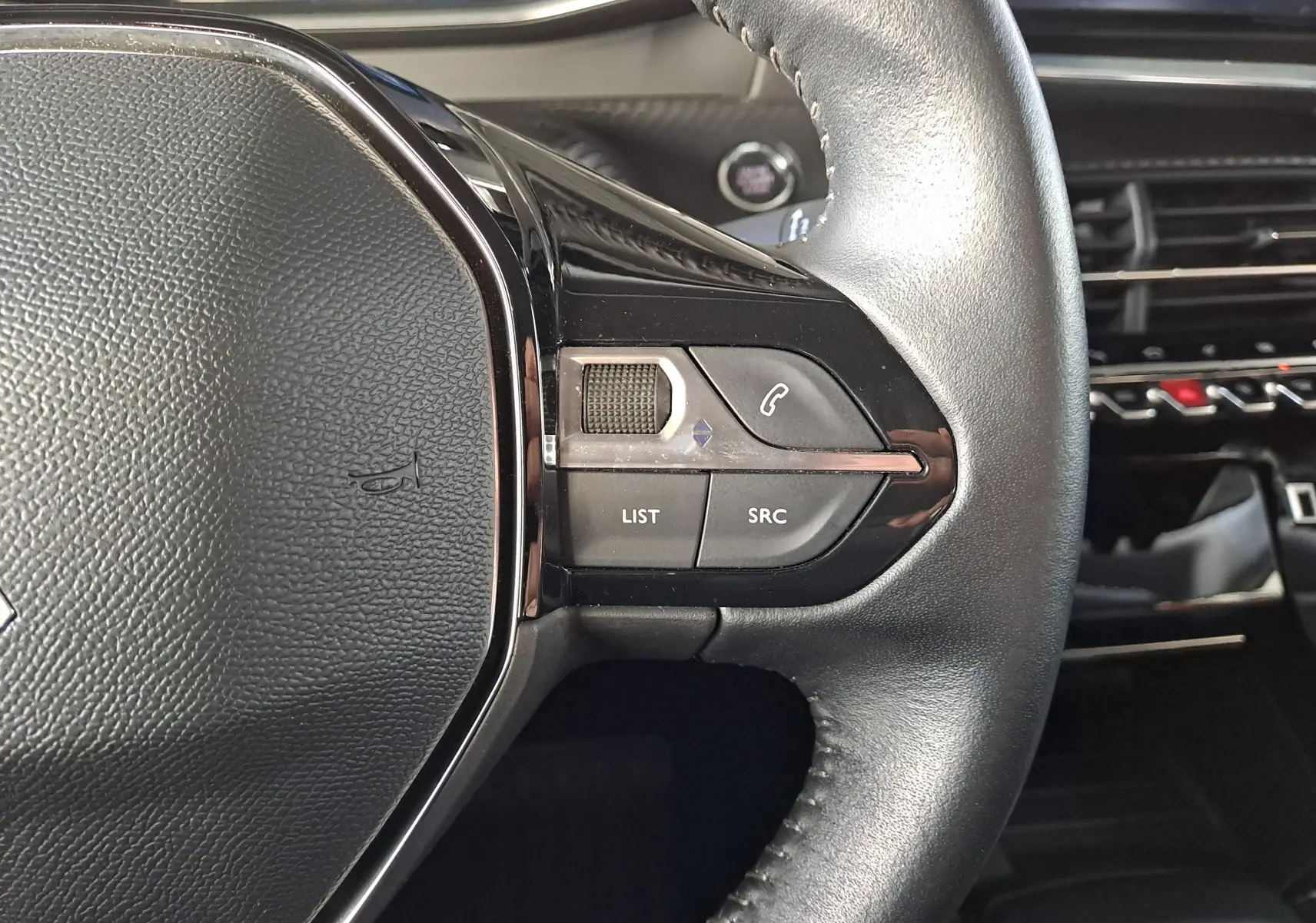 Gros plan sur le côté droit du volant en cuir noir du Peugeot 2008 1.2 PureTech 100 Allure, avec commandes intégrées.