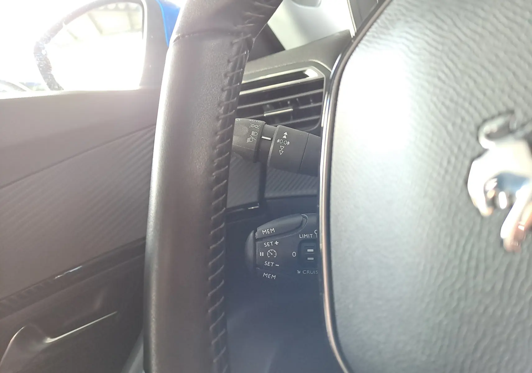 Gros plan sur le volant cuir noir du Peugeot 2008 bleu Vertigo, montrant les commandes de régulateur et lève-vitres côté gauche.