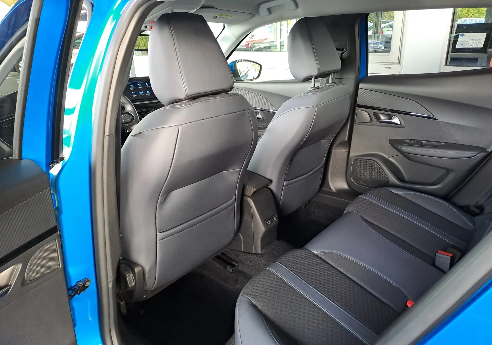 Vue intérieure arrière droite du Peugeot 2008 bleu Vertigo, montrant les sièges en tissu noir et détails modernes des portes.