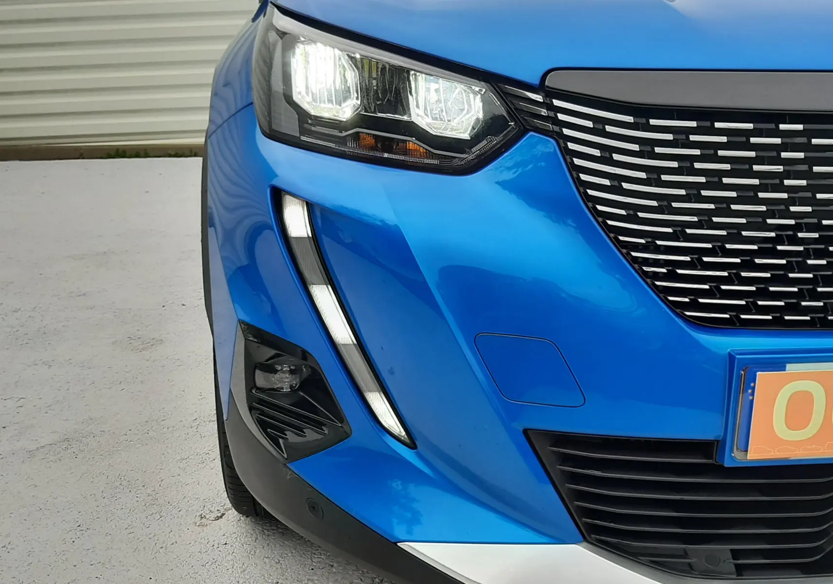 Gros plan sur l'avant gauche d'un Peugeot 2008 bleu Vertigo 2020, mettant en valeur son phare LED et sa calandre distinctive.