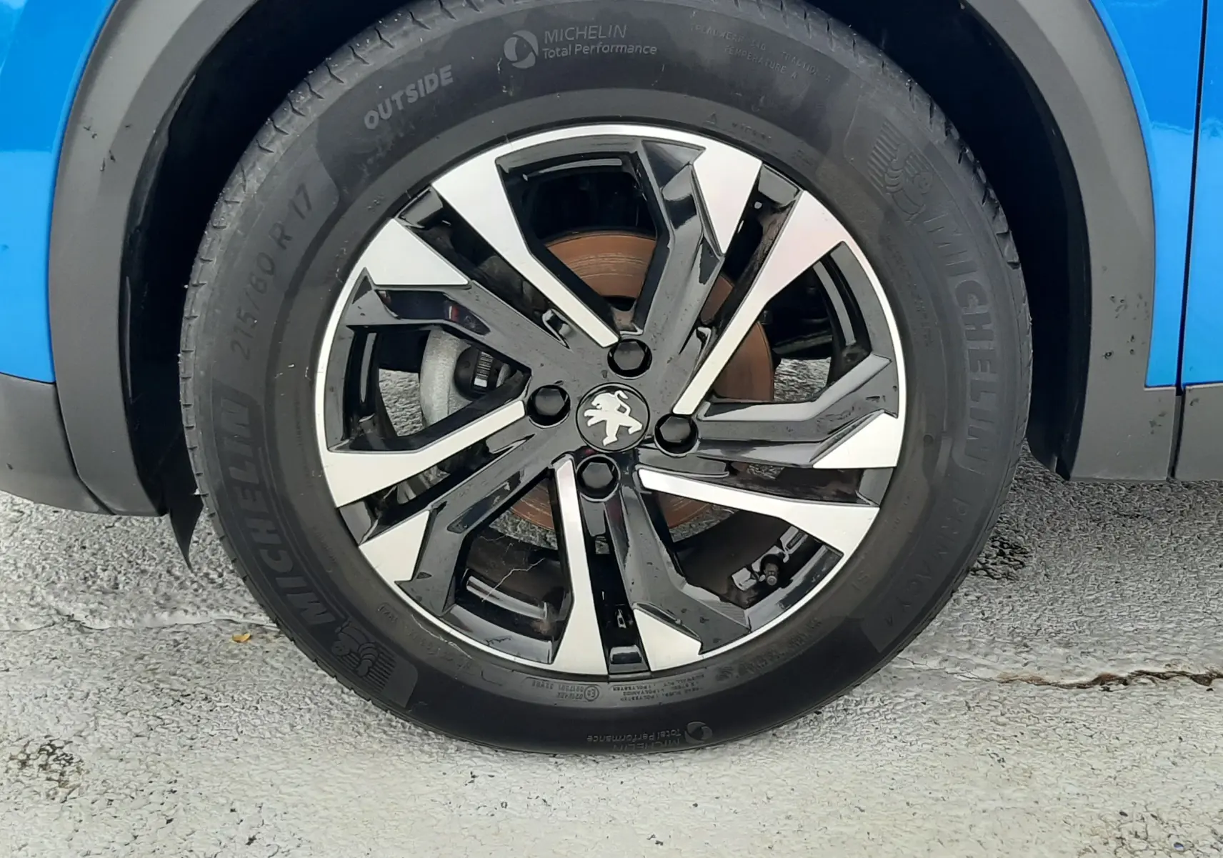 Gros plan sur la roue avant droite d'un Peugeot 2008 bleu Vertigo avec jante alliage noire et argentée.