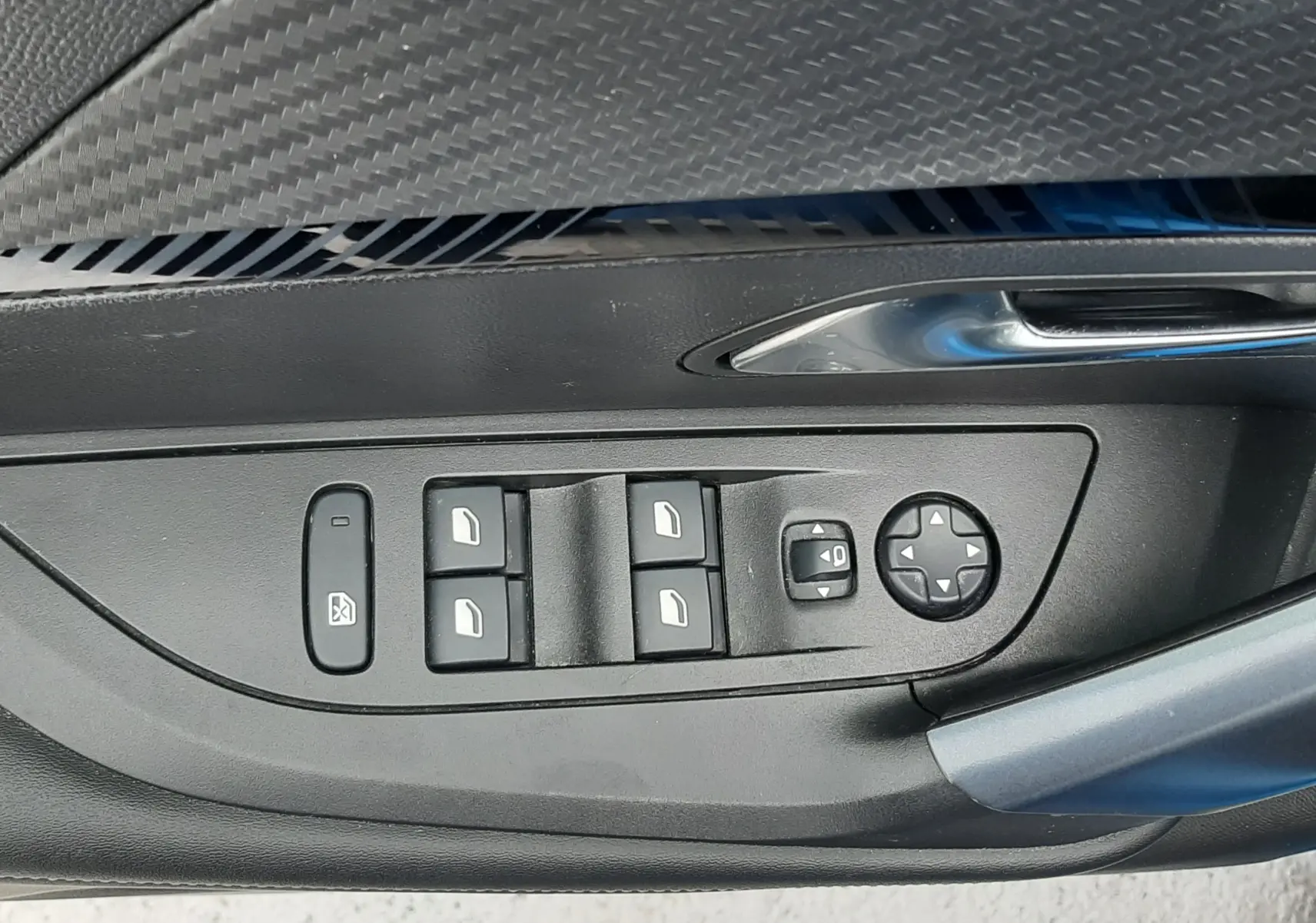Gros plan sur la commande des vitres et rétroviseurs côté conducteur d'une Peugeot 2008 bleu Vertigo, finition intérieure noire.