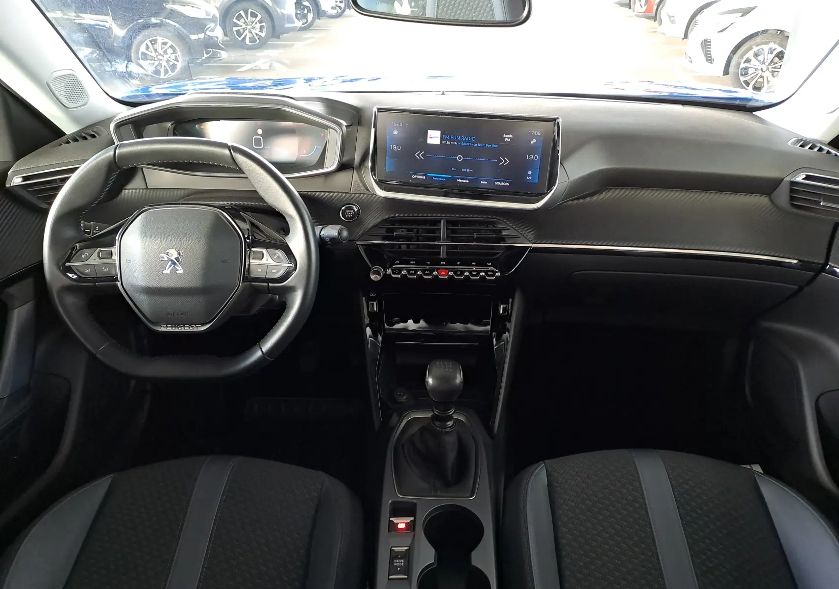 Vue intérieure frontale du tableau de bord et volant noir du Peugeot 2008 bleu Vertigo avec écran tactile et levier de vitesses manuel.