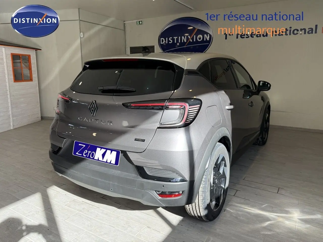 Vue 3/4 arrière droite du Renault Captur gris Cassiopée métal avec toit gris, en intérieur showroom, badge hybride visible.
