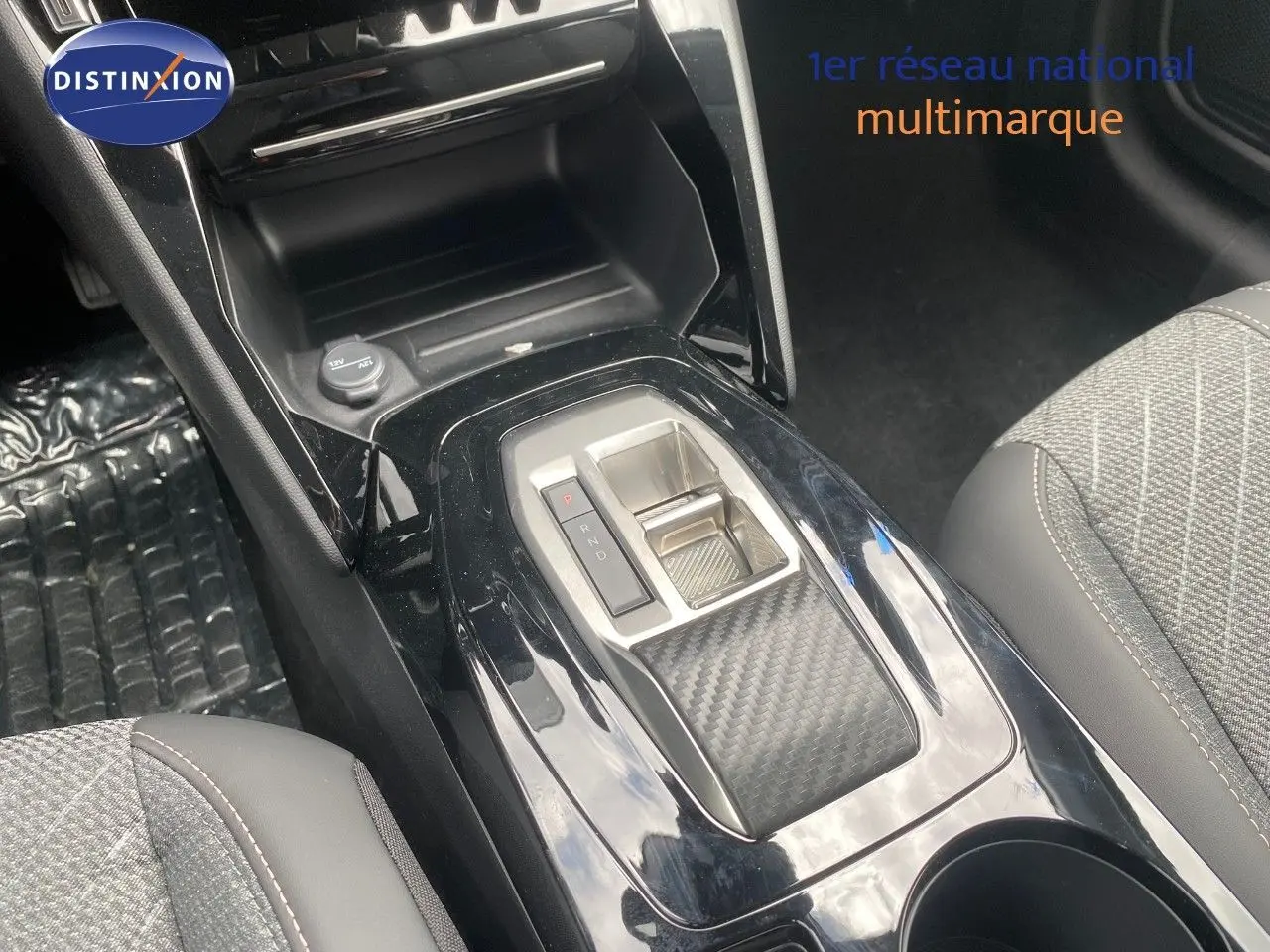 Vue rapprochée de la console centrale noire brillante avec sélecteur de boîte auto et sièges tissu gris de la Peugeot 208 Hybrid.