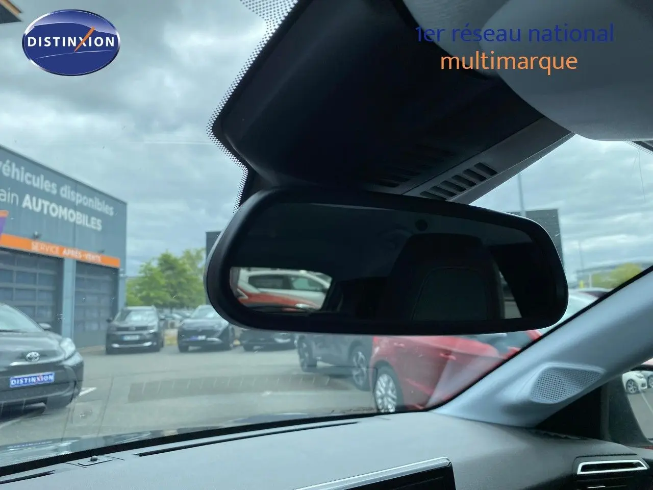 Vue intérieure du rétroviseur central d'une Peugeot 208 gris selenium métal, avec reflet du parking extérieur.