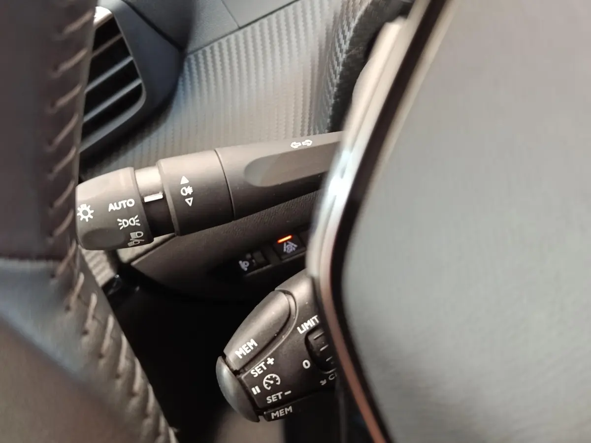 Gros plan sur la commande multifonctions noire du volant d'une Peugeot 208 2023, intérieur gris et noir.
