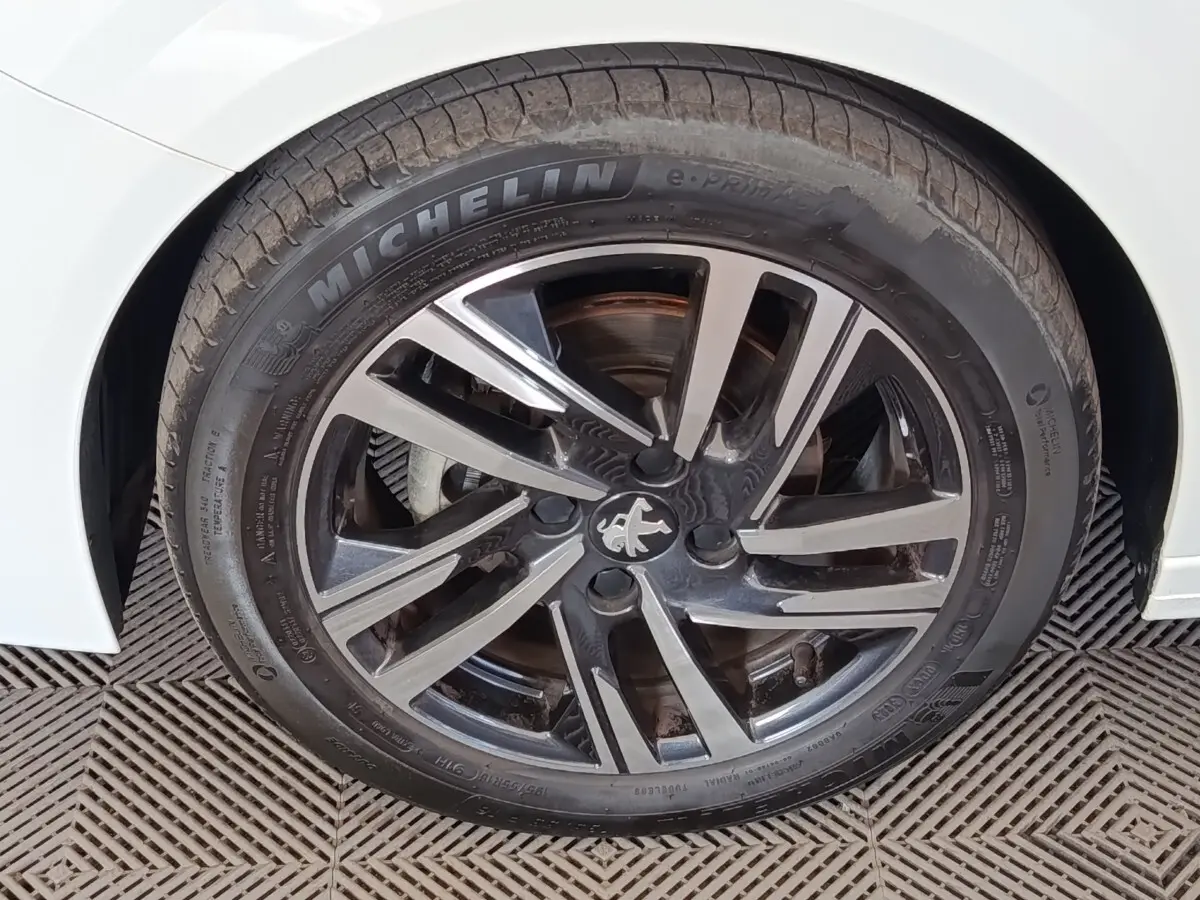 Gros plan sur la roue avant droite d’une Peugeot 208 blanche avec jante alliage noire et argentée au design moderne.