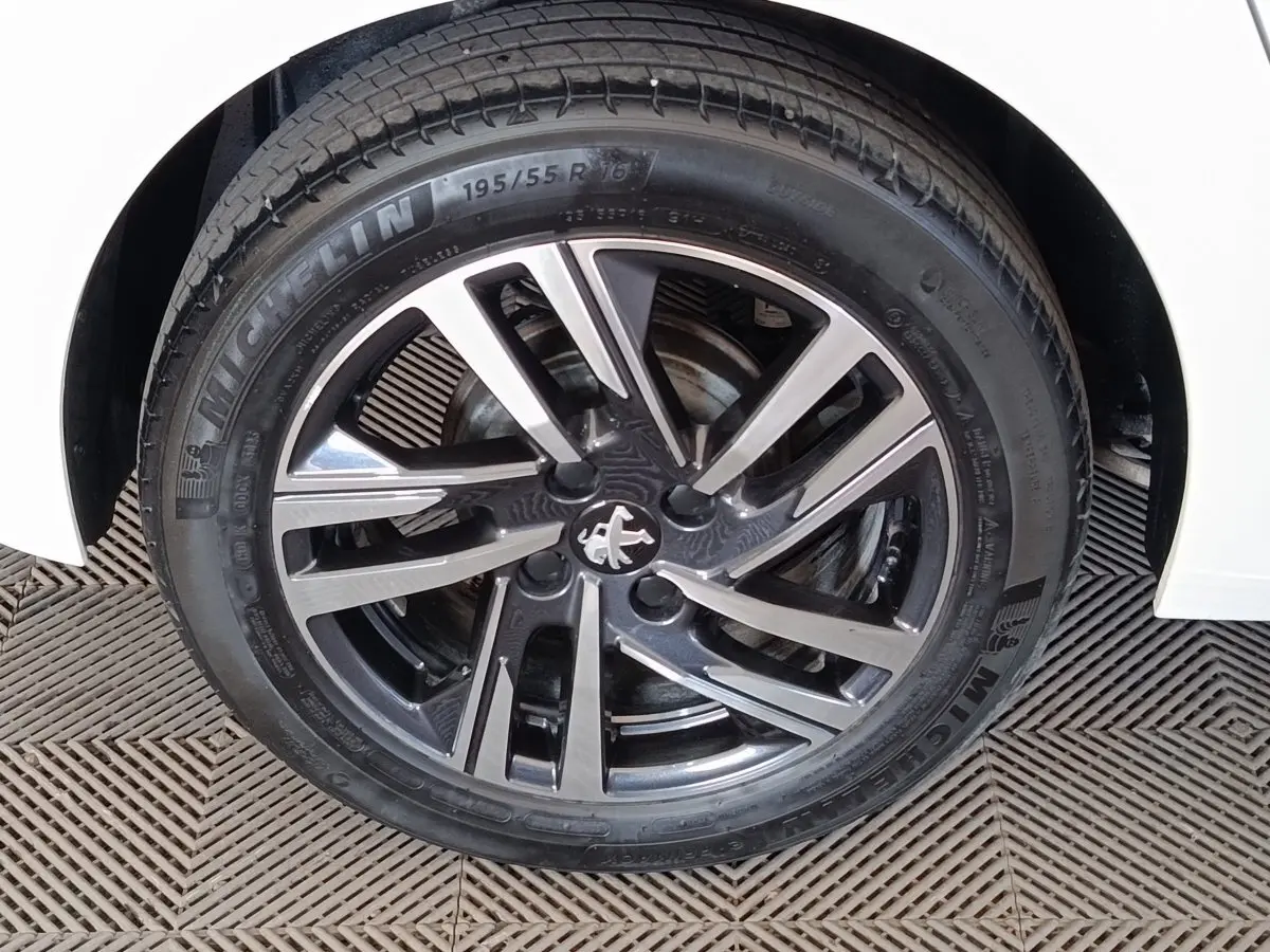 Gros plan sur la roue avant droite d'une Peugeot 208 blanche avec jante alliage bicolore et logo lion au centre.