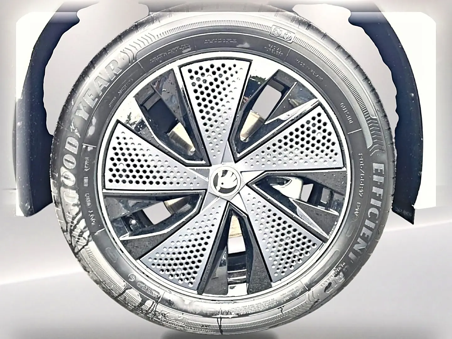 Gros plan sur la roue avant droite d’un Skoda Kamiq blanc nacré avec jante alu noire et argentée au design perforé.