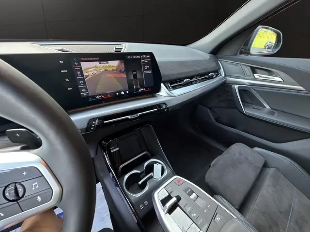 Vue intérieure côté conducteur du BMW X2 noir 2025, mettant en valeur l'écran tactile central et la console moderne.