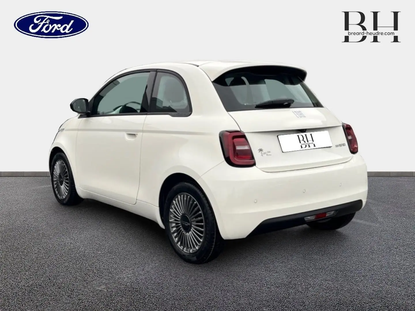 Vue 3/4 arrière droite de la FIAT 500 Ice White pastel avec jantes alu et becquet arrière visible sur fond neutre.