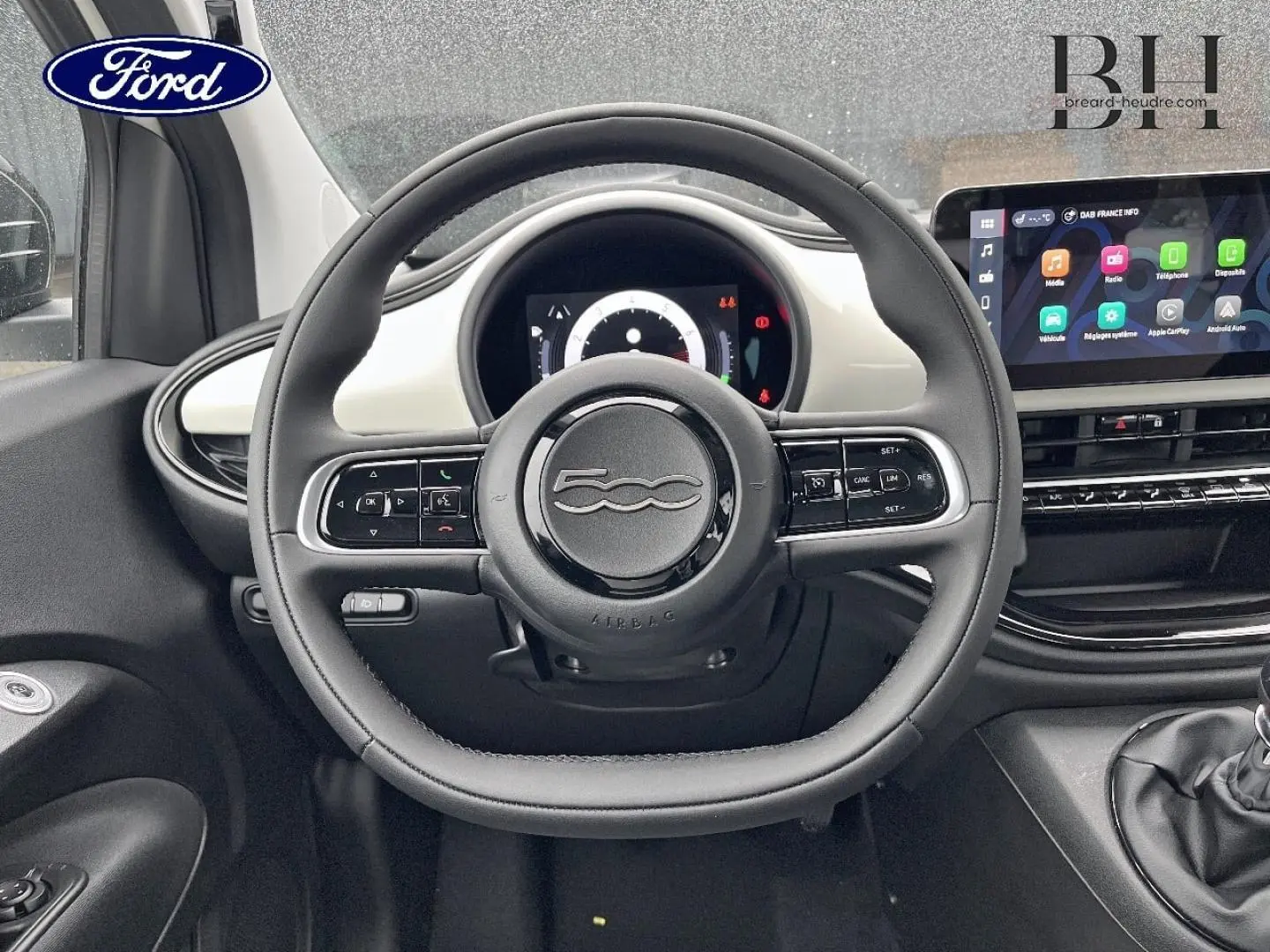 Vue intérieure centrée sur le volant de la Fiat 500 Ice White pastel avec tableau de bord et écran tactile visible.