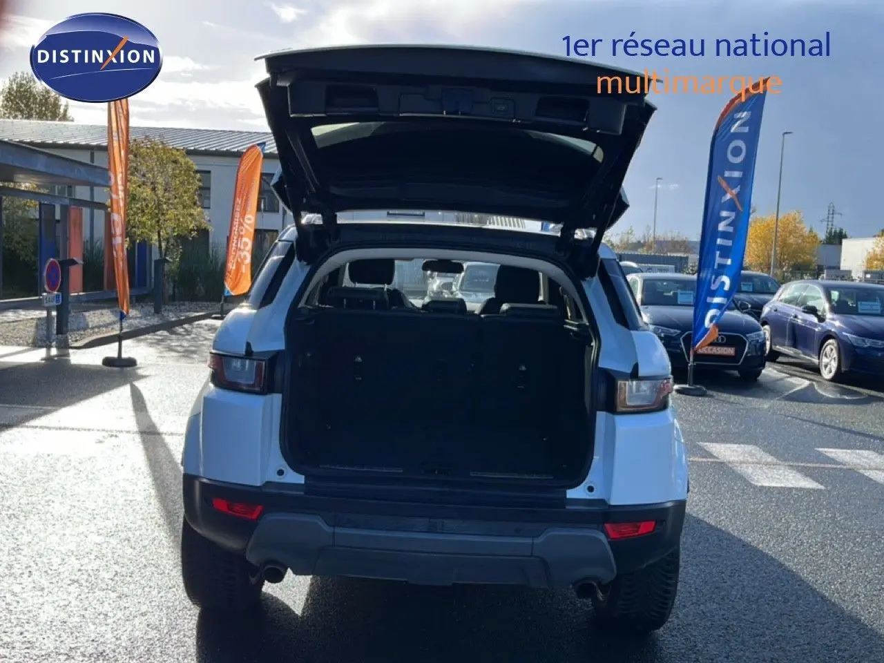 Vue arrière d'un Range Rover Evoque blanc 2017 avec coffre ouvert sur un parking ensoleillé.