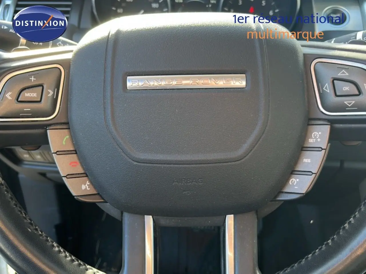 Gros plan sur le volant noir du Range Rover Evoque blanc, mettant en valeur les commandes intégrées et le logo central.