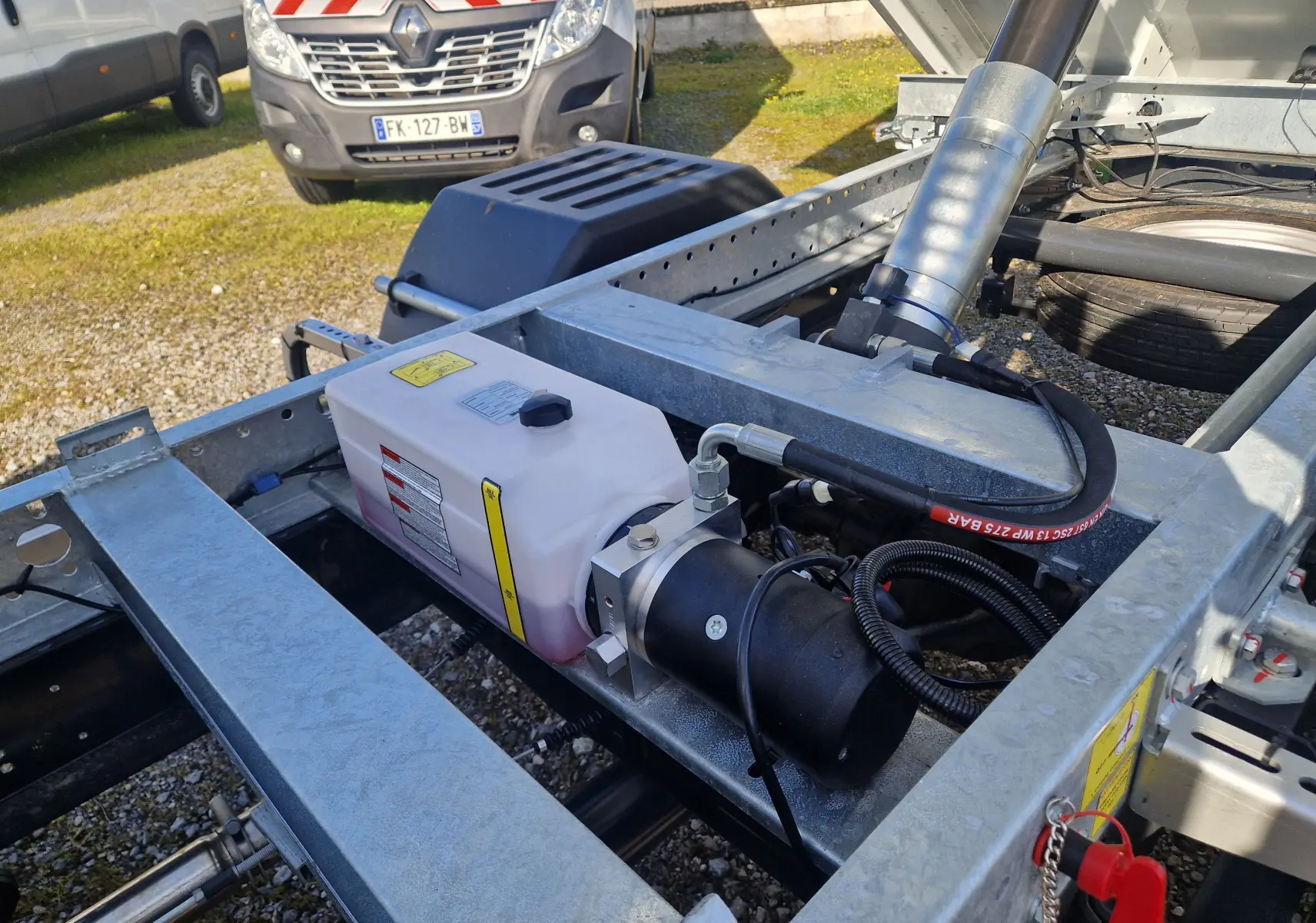 Gros plan sur le châssis métallique gris et le système hydraulique du benne blanc Iveco Daily 35C16, vue arrière droite.