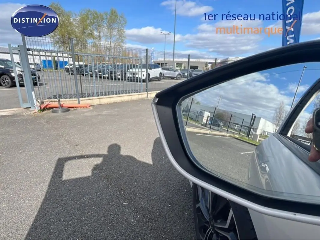 Rétroviseur droit d’une DS4 blanche 2024 avec reflet du ciel et d’un parking en arrière-plan.