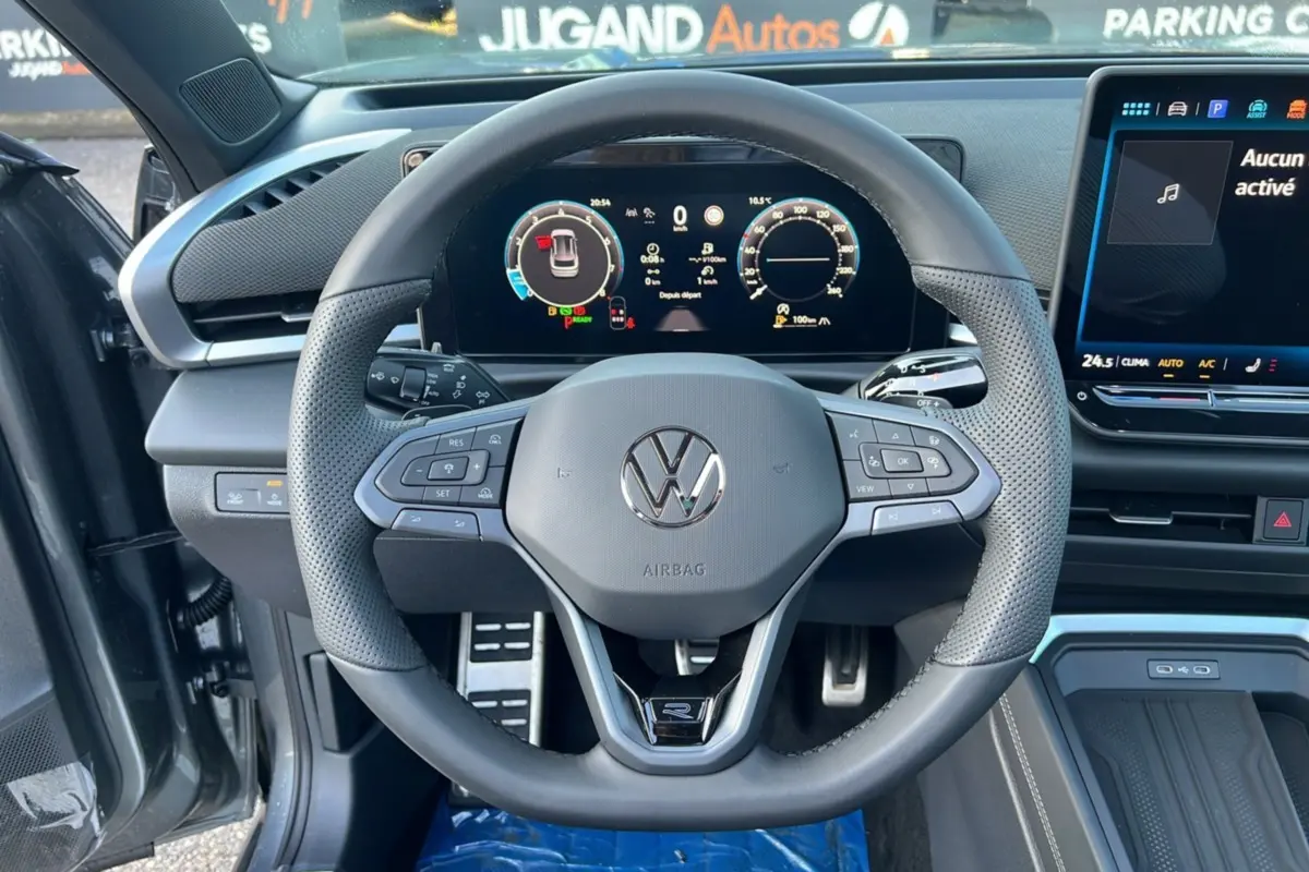 Vue intérieure centrée sur le volant cuir multifonctions du Volkswagen T-Roc gris loup avec tableau de bord digital et écran tactile.