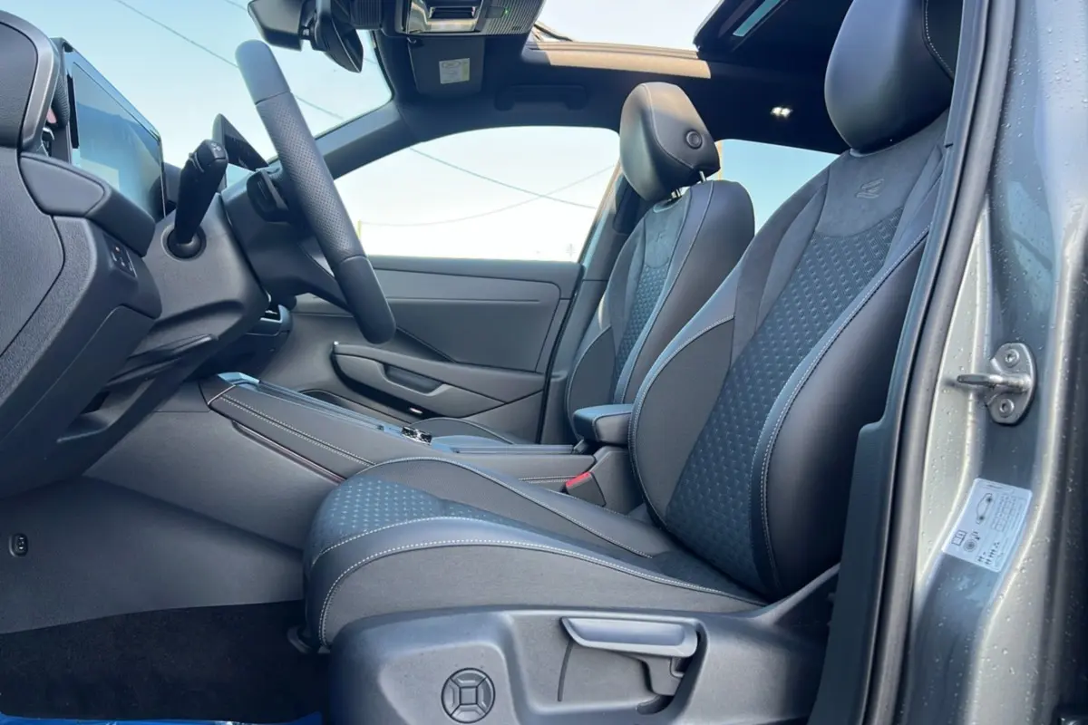 Vue intérieure côté conducteur du Volkswagen T-Roc gris loup 2026, sièges tissu R-Line avec surpiqûres blanches et toit ouvrant panoramique.