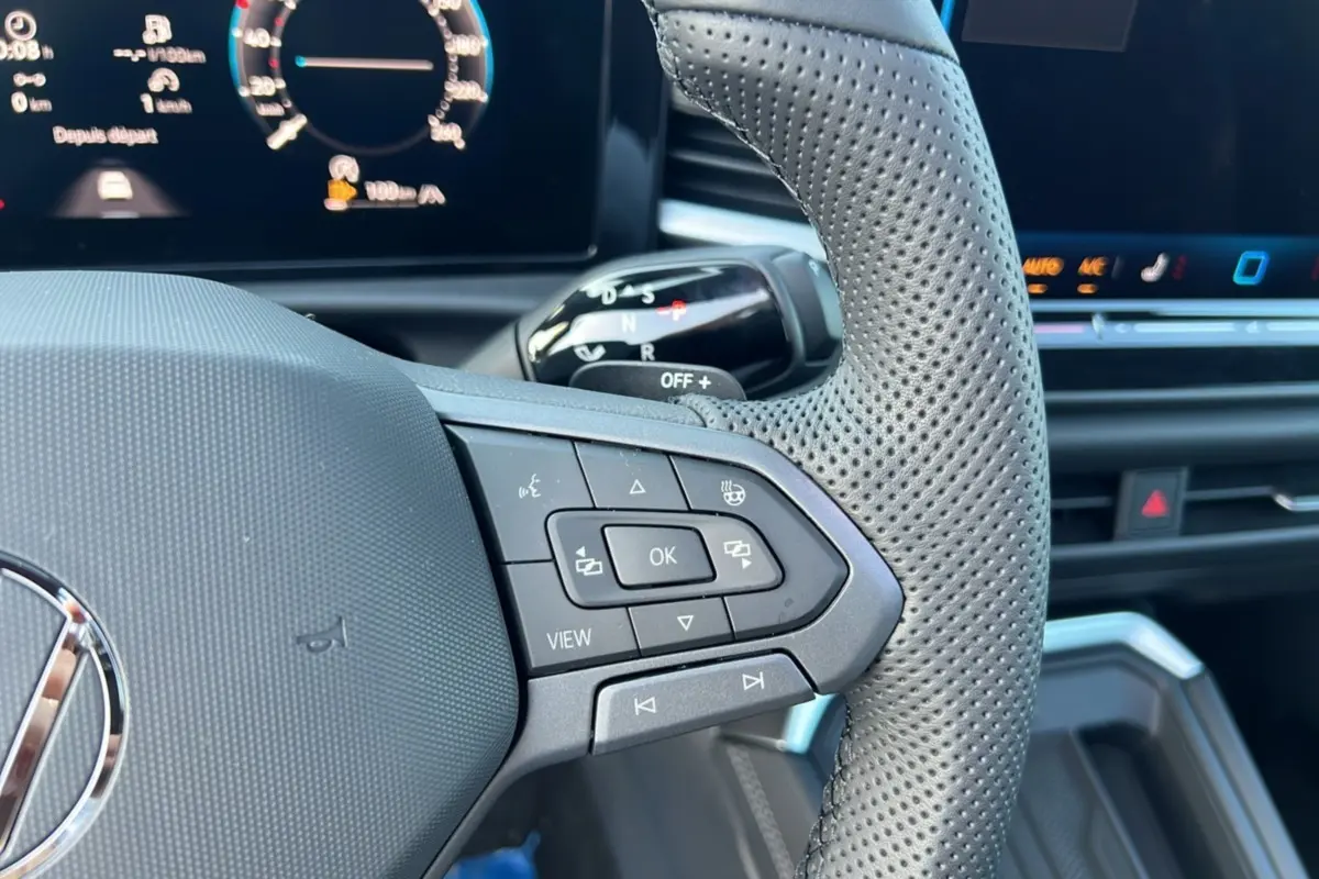 Gros plan sur le volant cuir perforé multifonctions côté droit du Volkswagen T-Roc gris loup avec tableau de bord digital.