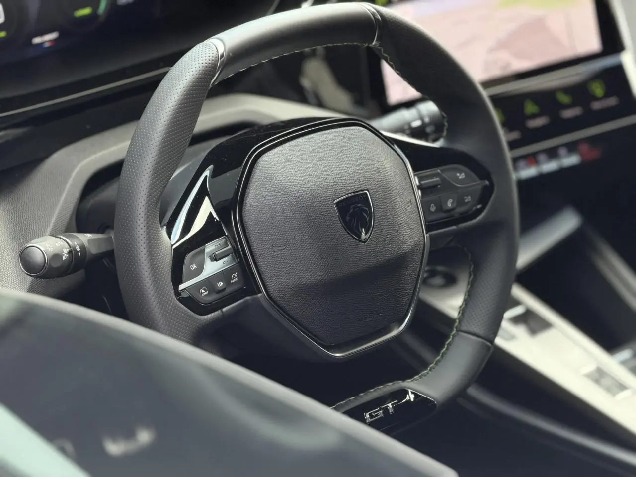 Gros plan sur le volant compact GT en cuir noir avec surpiqûres vert Adamite et logo Peugeot au centre.