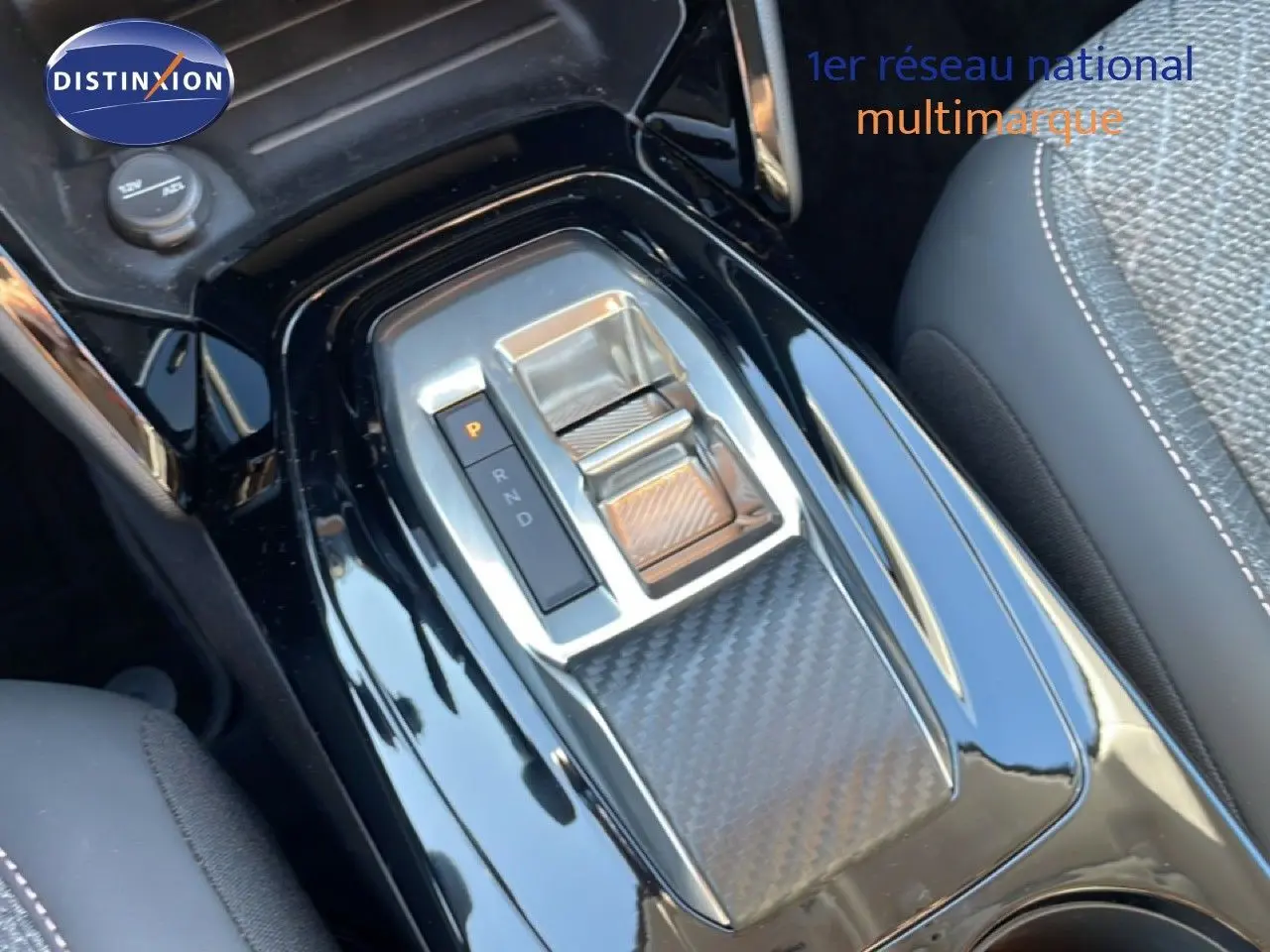 Gros plan sur la console centrale noire laquée de la Peugeot 208 Hybrid 110ch, avec levier de boîte automatique et finition carbone.